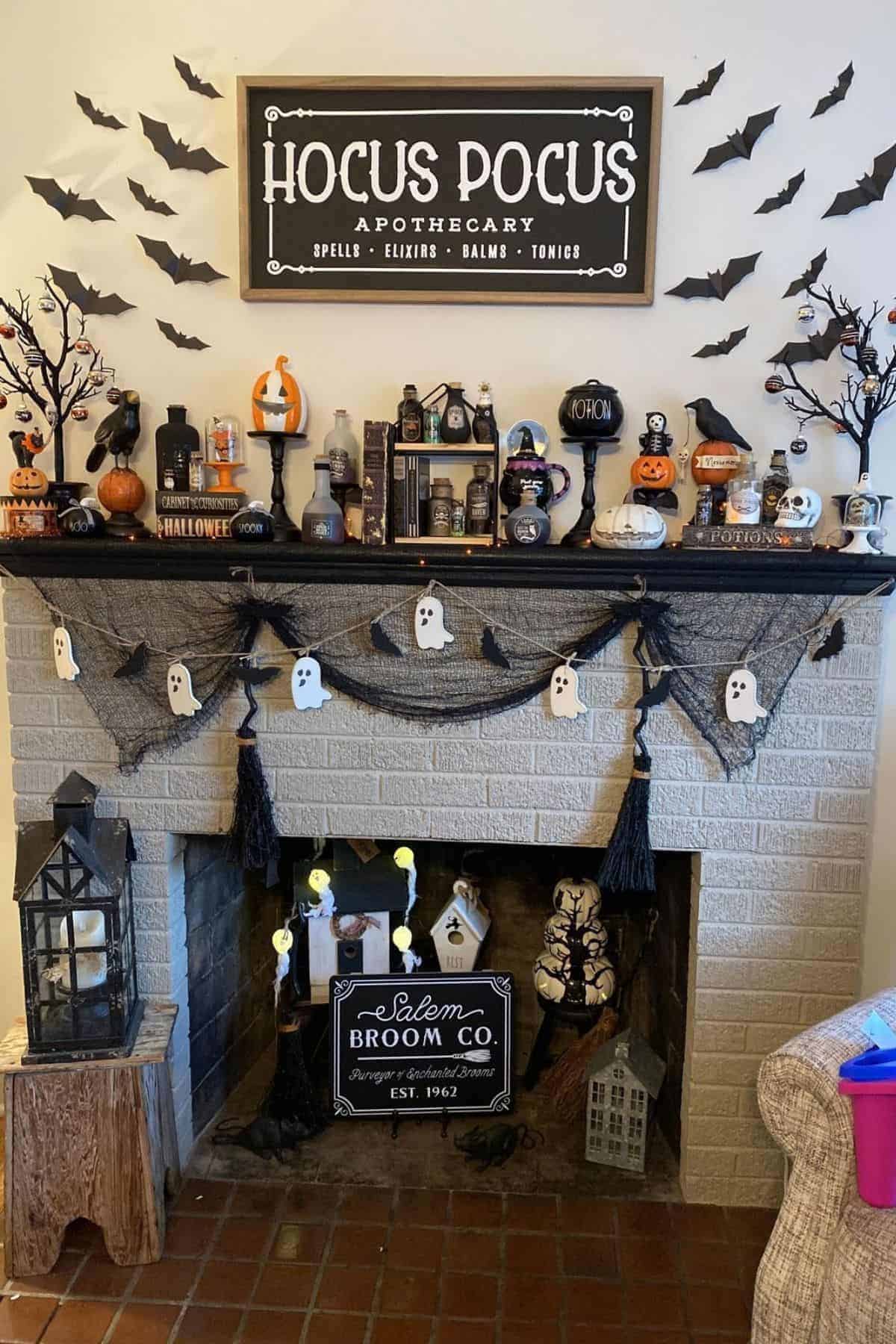 A fireplace decorated for Halloween with a “Hocus Pocus Apothecary” sign, bats, pumpkins, potion bottles, ghosts garland, and other themed ornaments on the mantel and around the hearth.