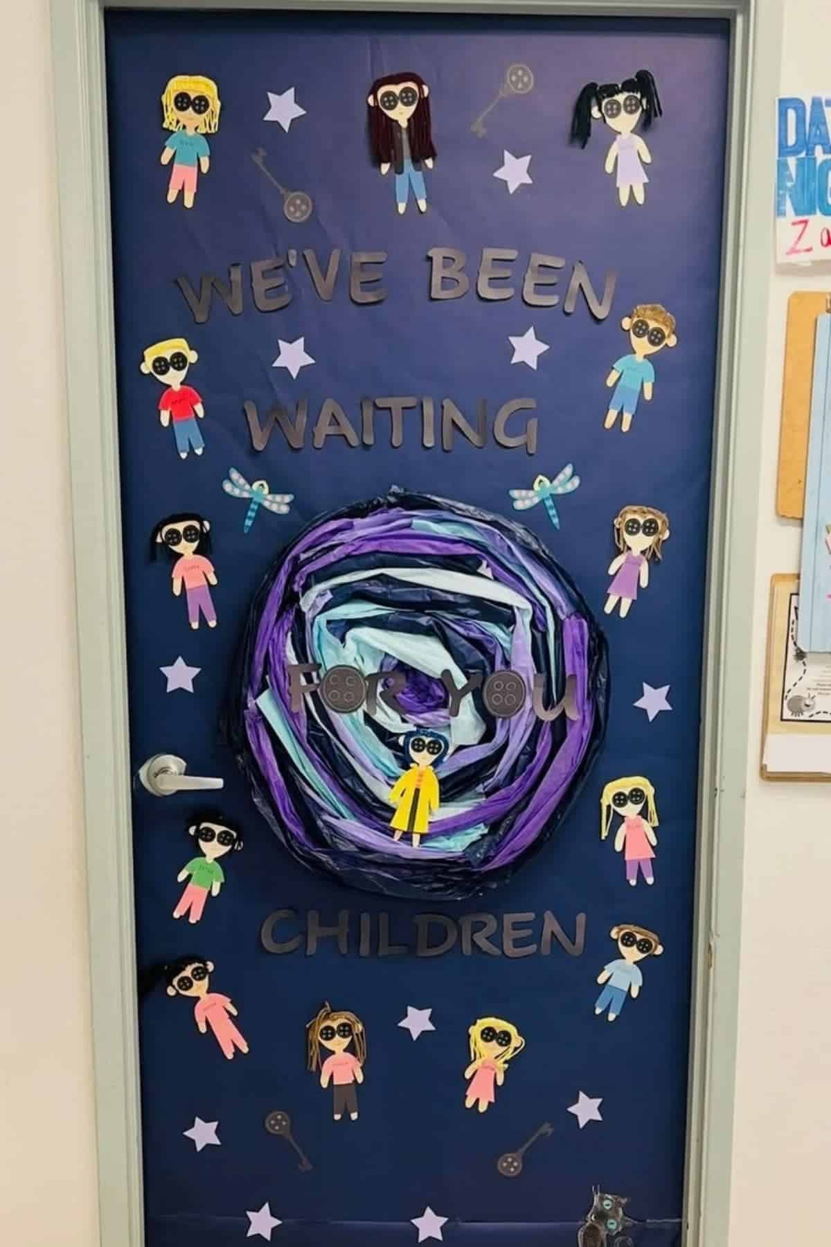 Classroom door decorated with paper children, stars, and a swirling portal; text reads, “We’ve been waiting for you children.”.
