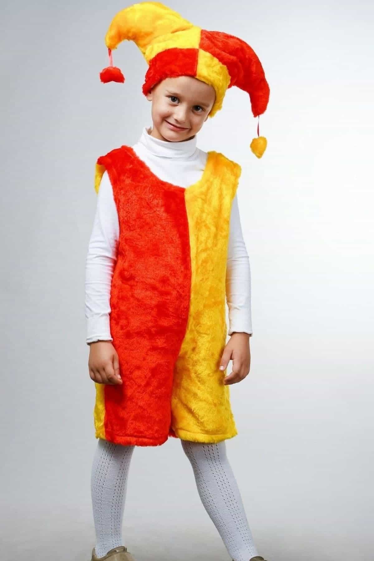 A child wearing a red and yellow jester costume, including a hat with two points and pom-poms, stands against a plain light background.