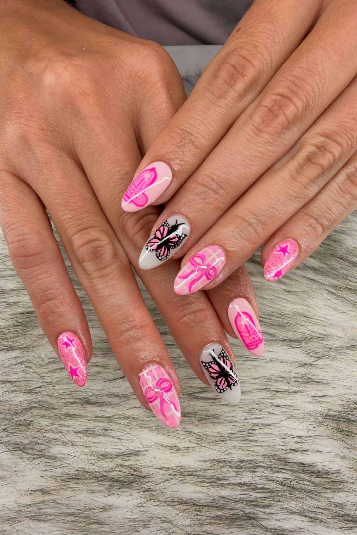 Hands with long nails painted pink and white, decorated with butterflies, ribbons, and stars, resting on a gray and white textured surface.
