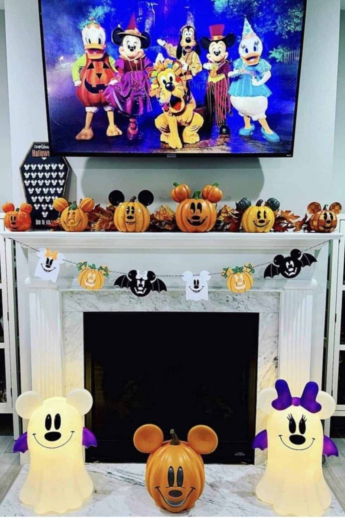 A TV displays Disney characters in Halloween costumes above a fireplace decorated with pumpkin figures, ghost and bat garlands, and two Mickey and Minnie Mouse light decorations.