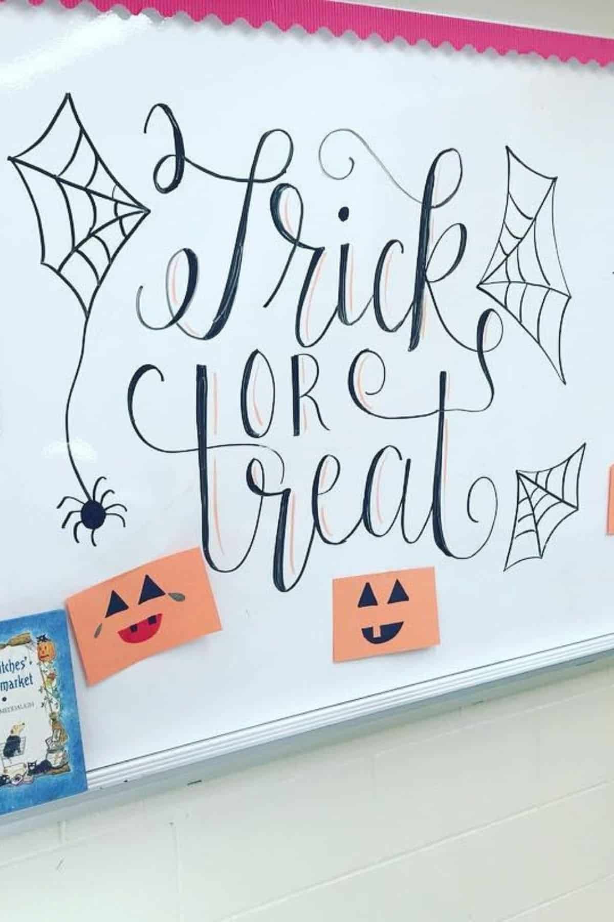 Whiteboard with “Trick or Treat” written in cursive, decorated with spider webs, a spider, and orange paper pumpkins with faces.
