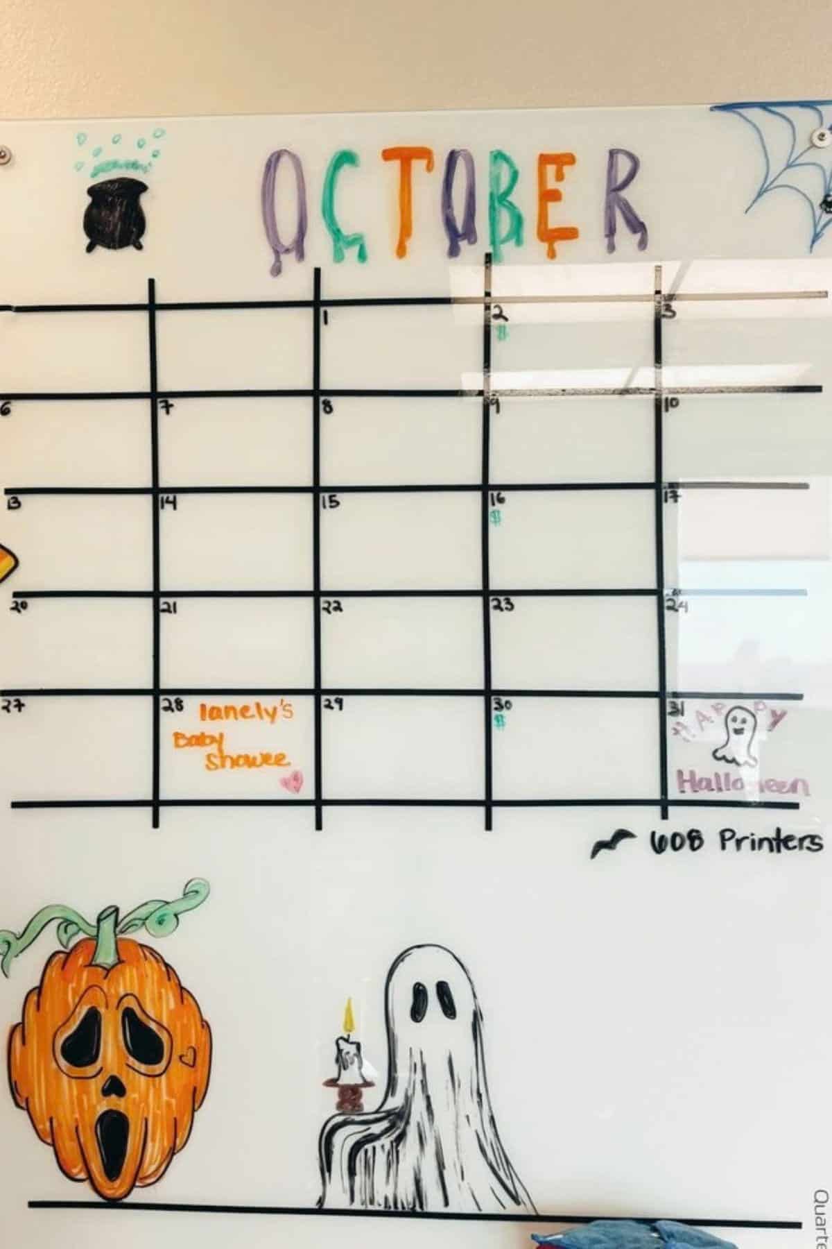 A whiteboard calendar for October is decorated with Halloween-themed drawings, including a pumpkin and ghost. Some dates are labeled, such as “baby shower” and “Halloween.”.