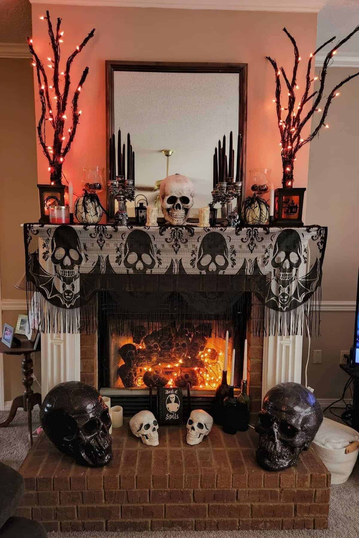 A fireplace decorated with skulls, black candles, and orange-lit tree branches, creating a Halloween-themed display.