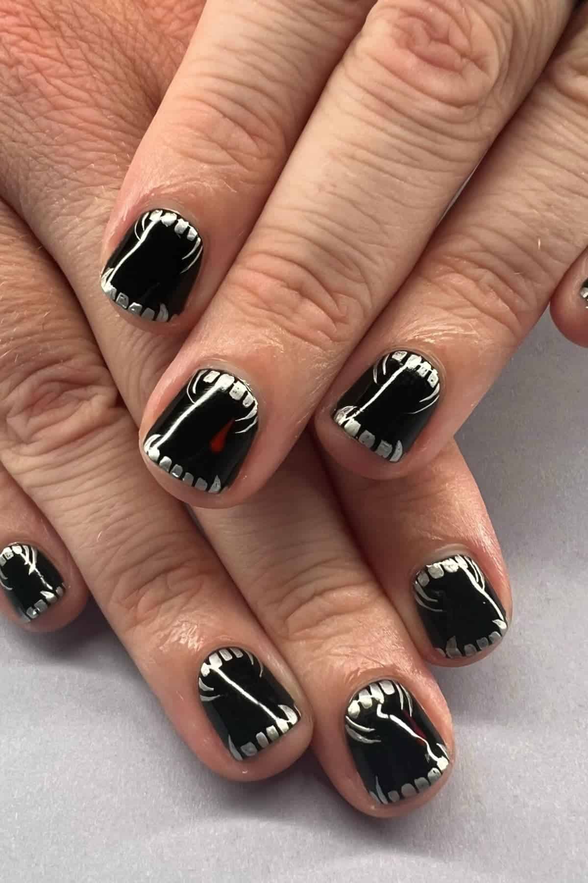 Fingernails painted with black polish and white designs resembling open mouths with teeth.