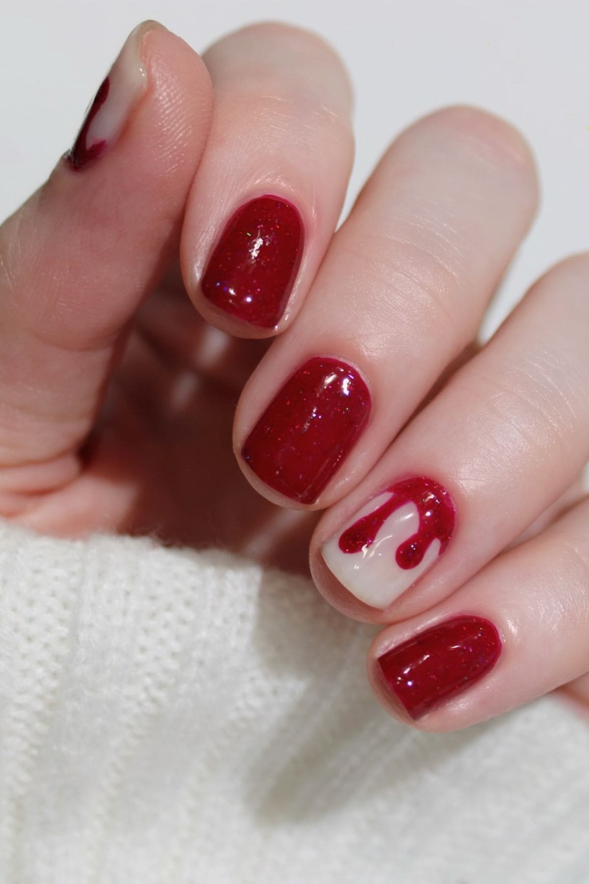 A hand with short nails painted dark red; the ring finger has a heart-shaped red and clear design.