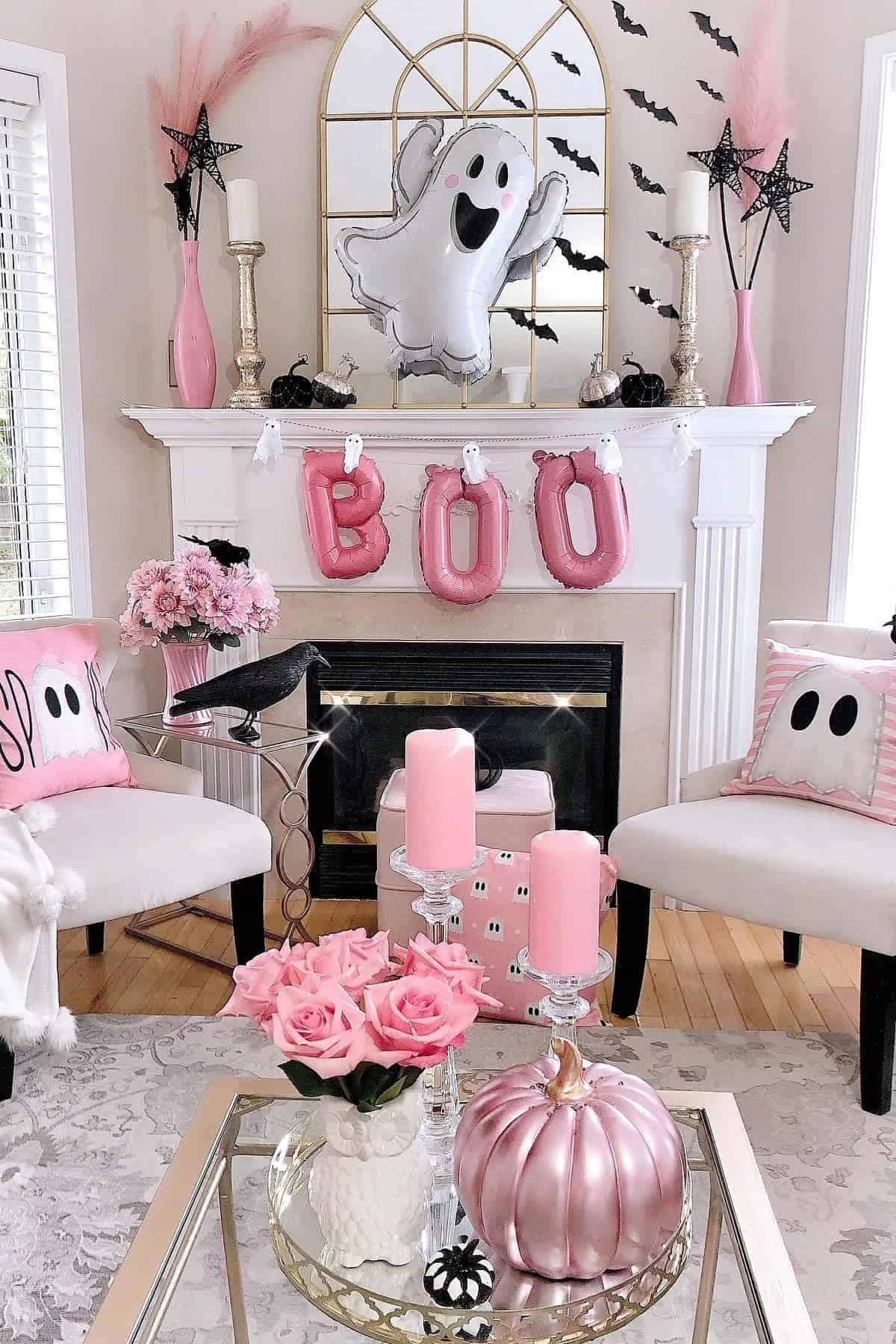 A living room decorated for Halloween with pink accents, ghost and “BOO” balloons, pink candles, a pink pumpkin, roses, bats, and themed pillows arranged around a white fireplace.