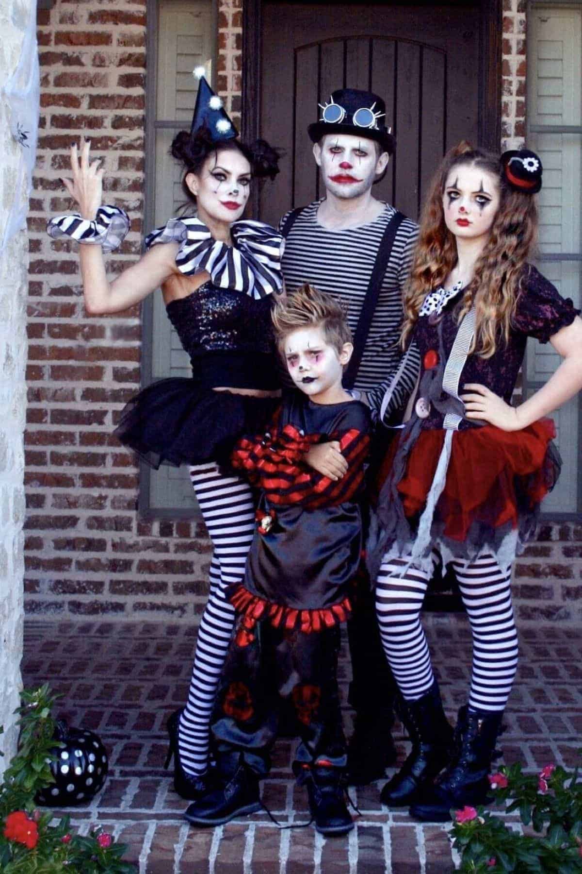 Four people in matching black, white, and red clown costumes with face paint stand on a brick porch in front of a door.
