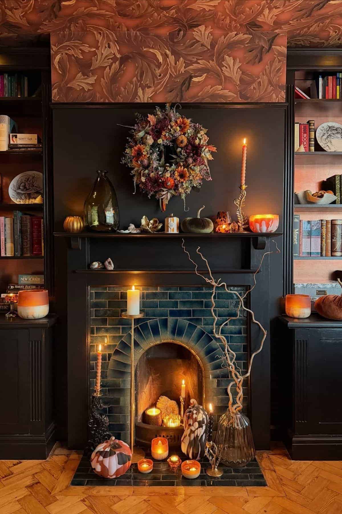 A decorated fireplace with candles, pumpkins, a floral wreath, and autumn-themed ornaments arranged on and around the mantel in a dimly lit room.