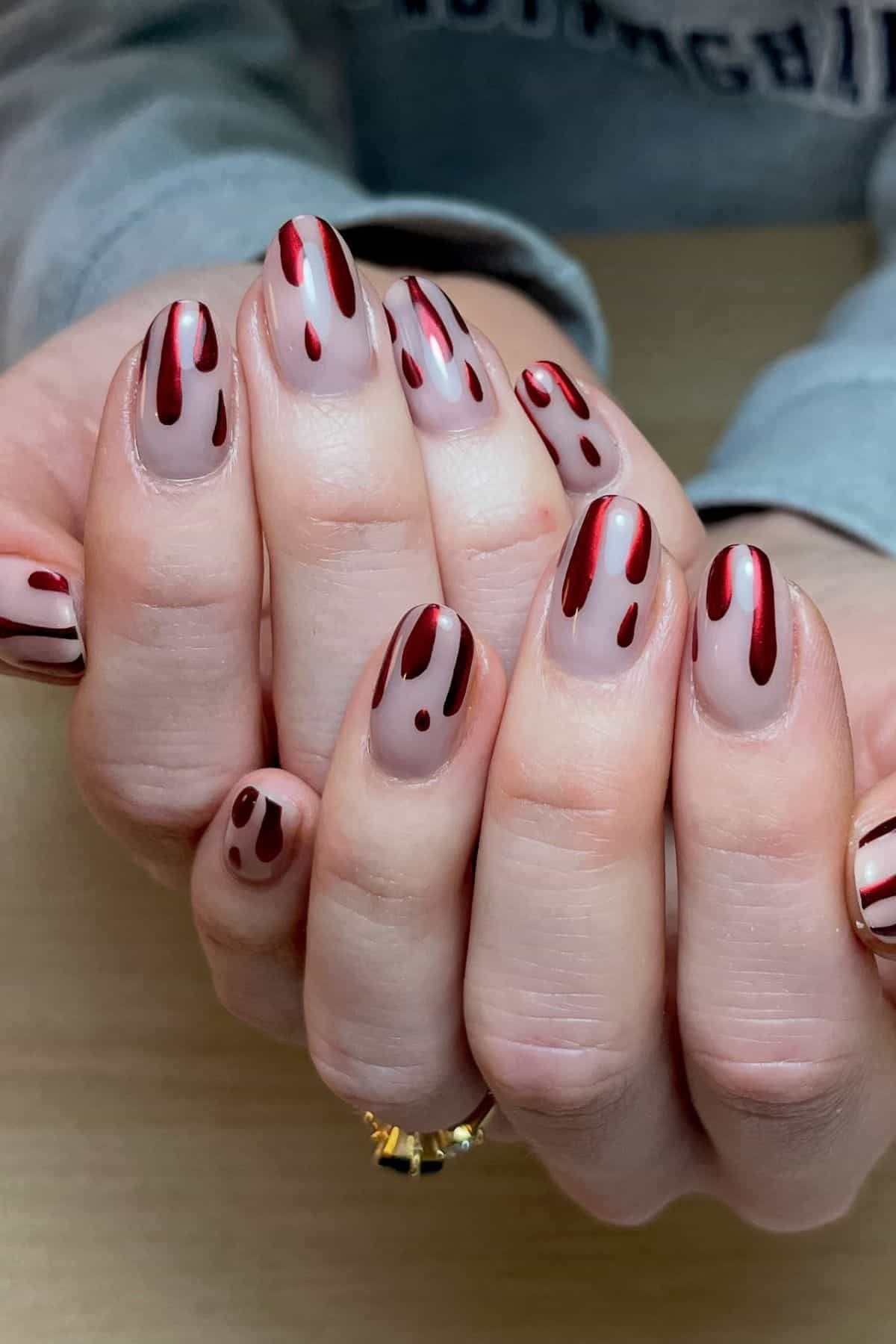 Hands with manicured nails, featuring a nude base and red abstract vertical stripes and dots.