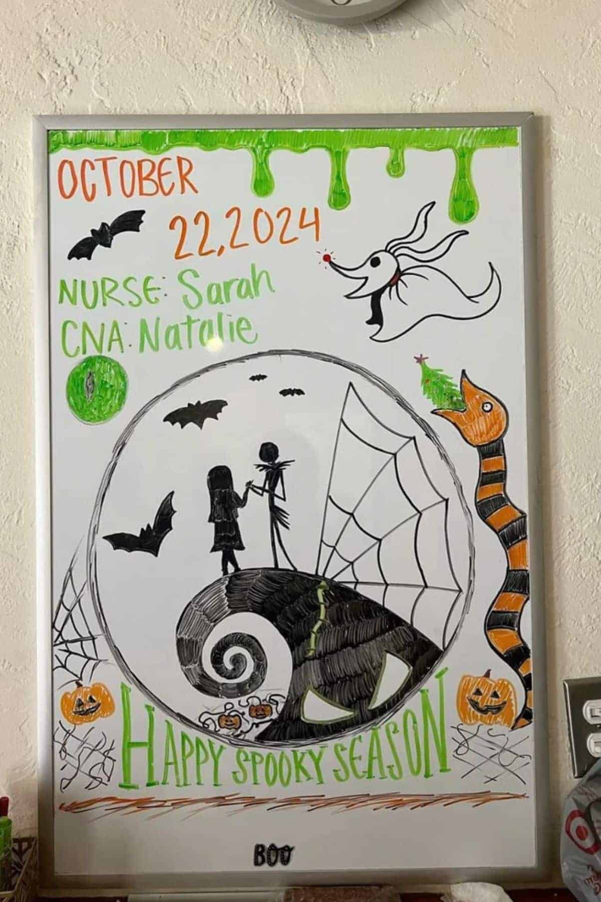 Whiteboard with Halloween-themed drawings, date October 22, 2024, nurse Sarah, CNA Natalie, and “Happy Spooky Season” text, with bats, pumpkins, and cartoon characters.