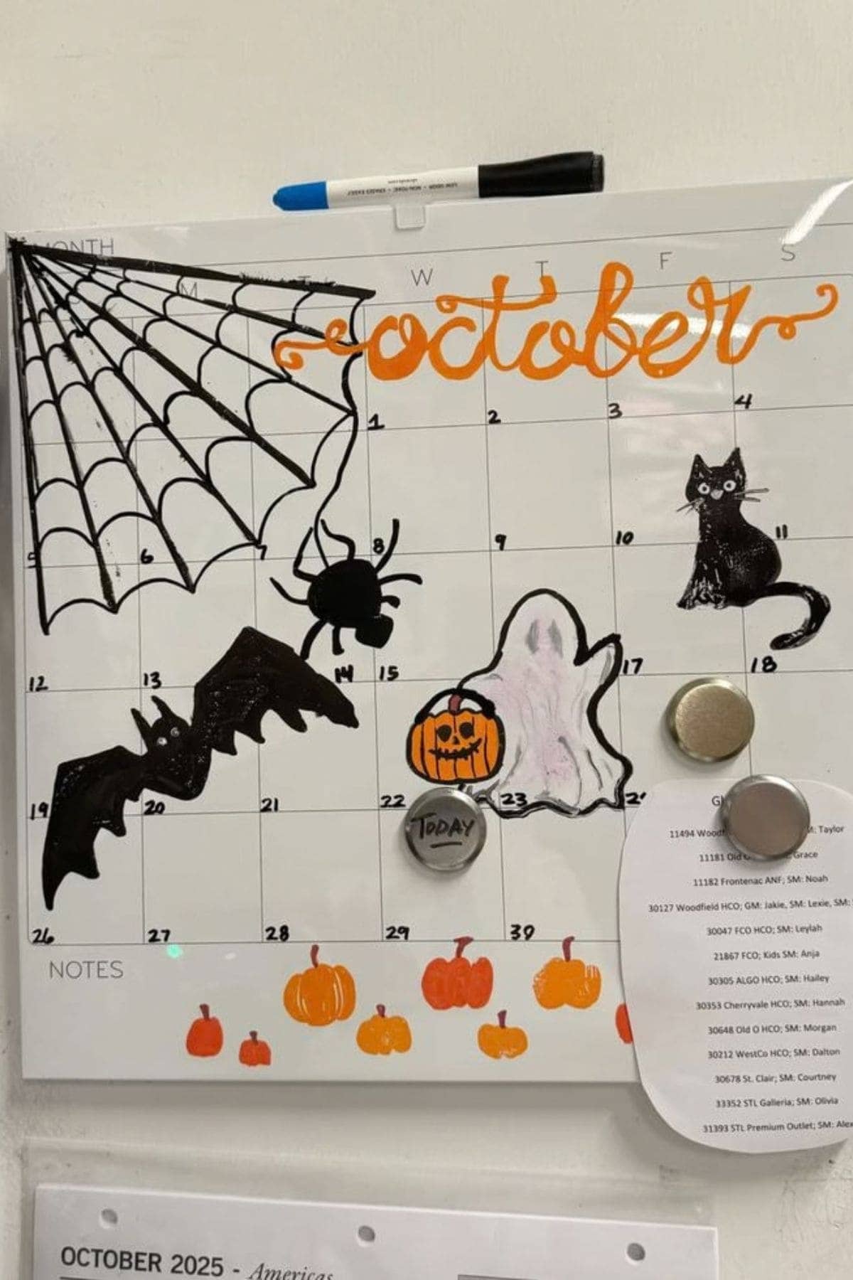 A whiteboard calendar for October is decorated with Halloween-themed drawings, including a bat, spider, web, cat, ghost, pumpkins, and a pumpkin with a face.
