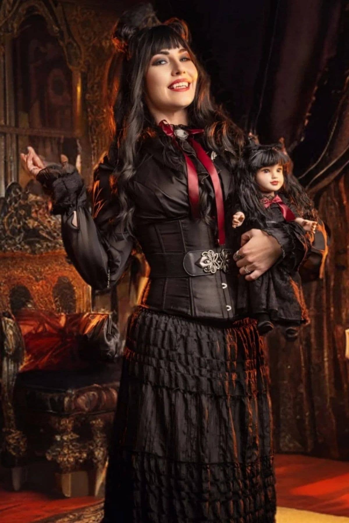 Woman in a black Victorian-inspired outfit holding a matching doll, standing in a lavish room with ornate carved furniture.