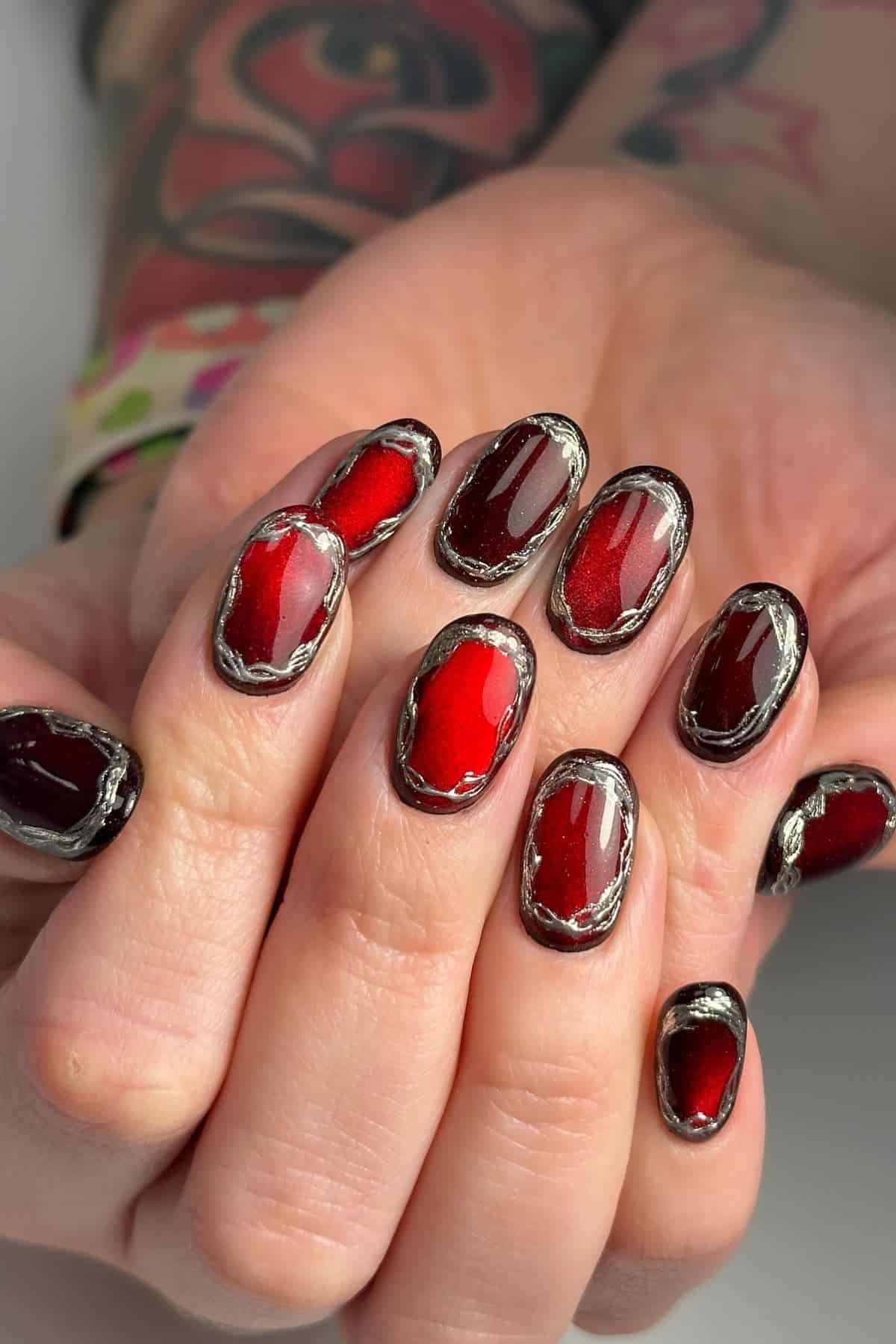 Close-up of hands with oval-shaped nails painted in dark red polish, bordered with metallic silver accents.