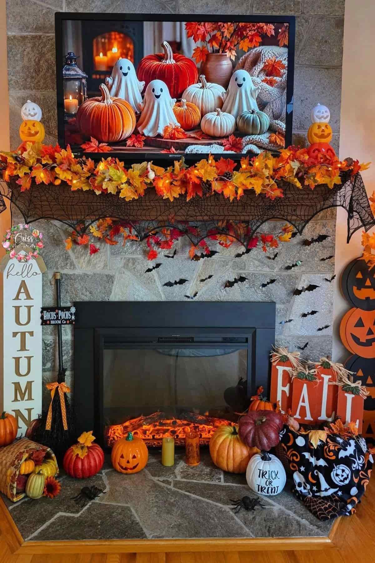 A fireplace decorated for Halloween and autumn with pumpkins, jack-o’-lanterns, leaves, signs, and ghost decorations; a TV above displays similar fall-themed decor.