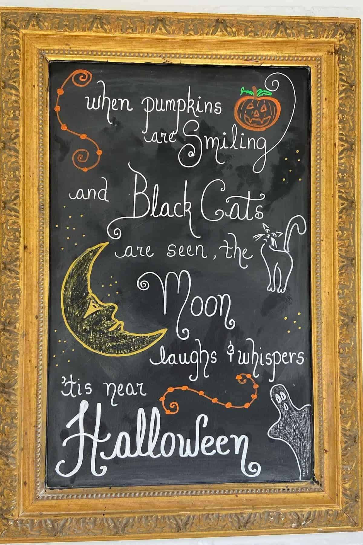 Framed chalkboard with Halloween-themed drawings and text about pumpkins, black cats, and the moon, with images of a pumpkin, cat, moon, stars, and ghost.