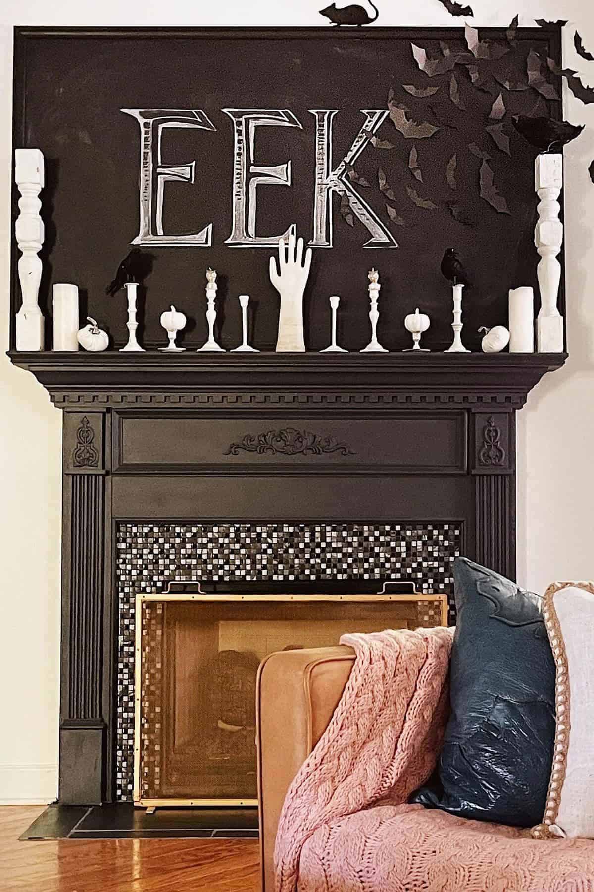 A black fireplace mantel decorated with white candles, candlesticks, a hand sculpture, black birds, and the word “EEK” on a black backdrop for Halloween.