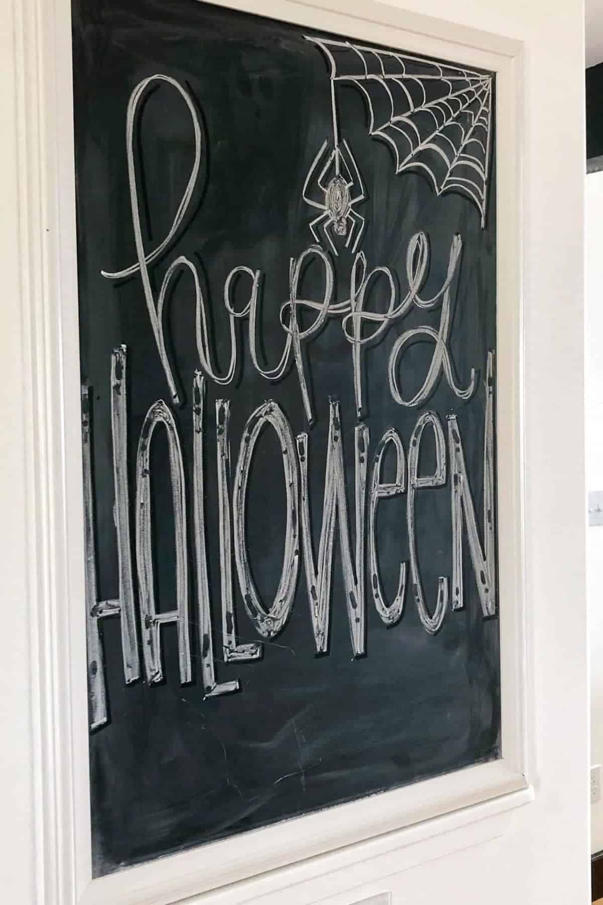 A chalkboard with “Happy Halloween” written in large letters, decorated with a spider and a spiderweb drawn in the top right corner.