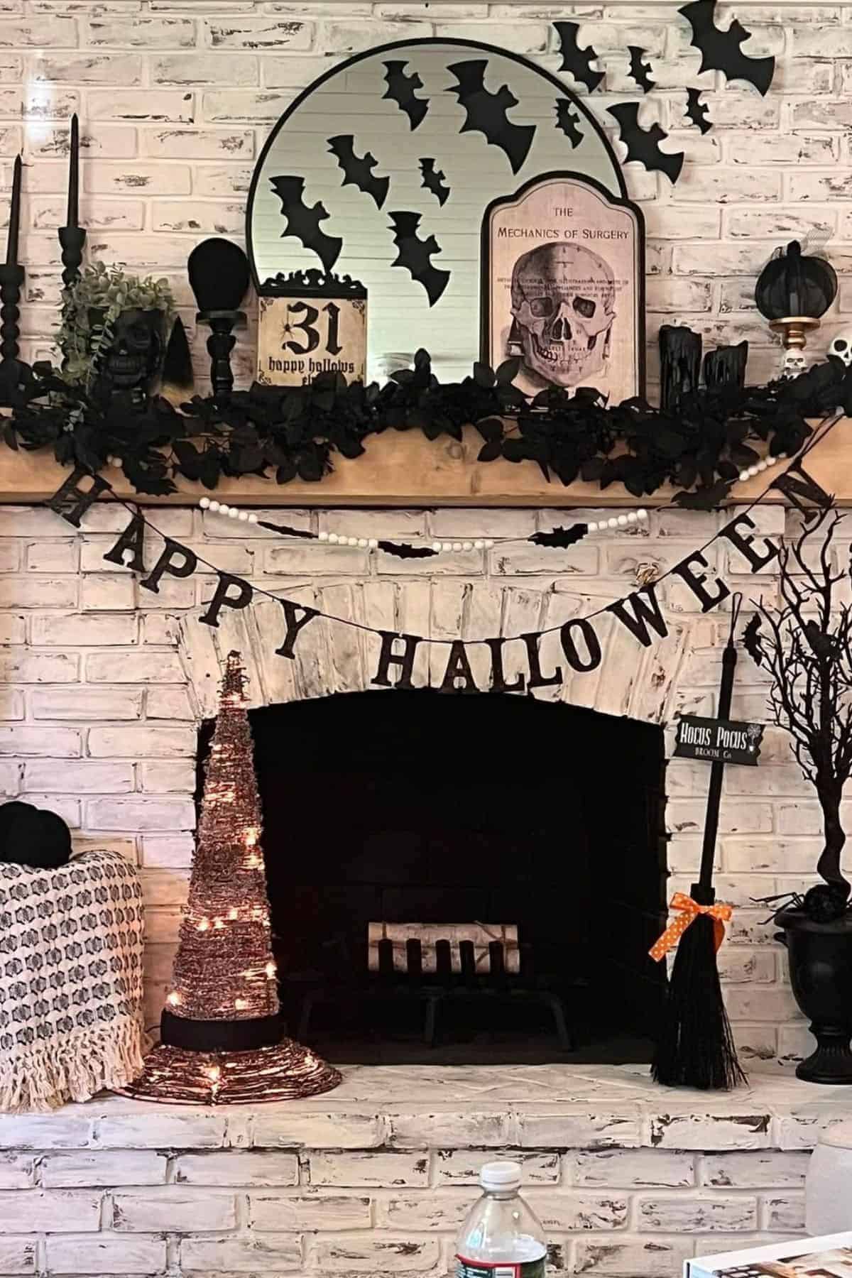 A decorated fireplace with Halloween props, including black bats, a skull book, black garland, candles, a witch hat, broom, and a “Happy Halloween” banner.