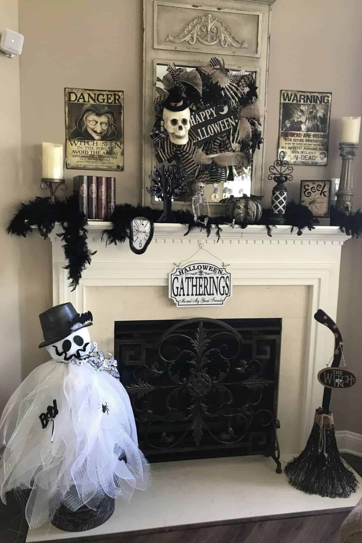 A fireplace decorated for Halloween with skulls, gothic accessories, black garland, spooky signs, a broom, and a ghost figure in a white dress and hat.