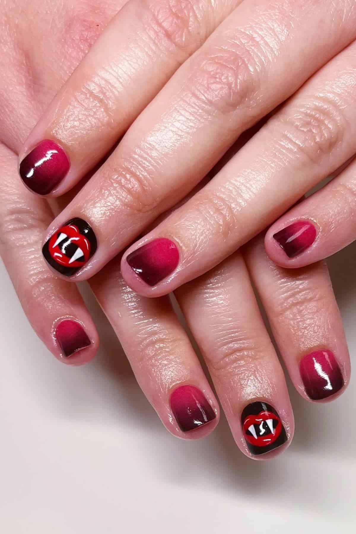 Hands with short, red-gradient manicure; ring fingers feature a design of vampire fangs inside a red mouth on a black background.