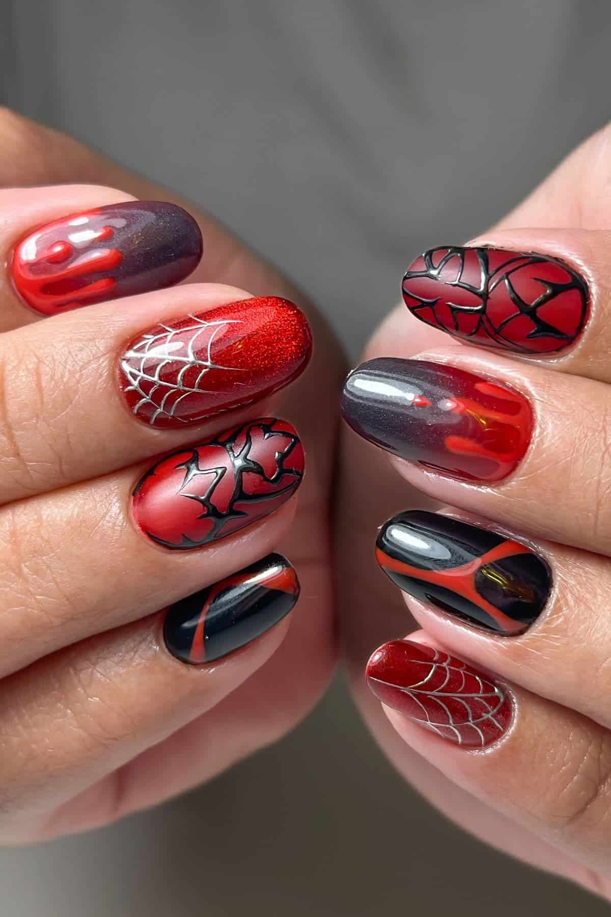 Hands with manicured nails featuring red, black, and gray polish, decorated with spider web, crackle, and abstract designs on each nail.