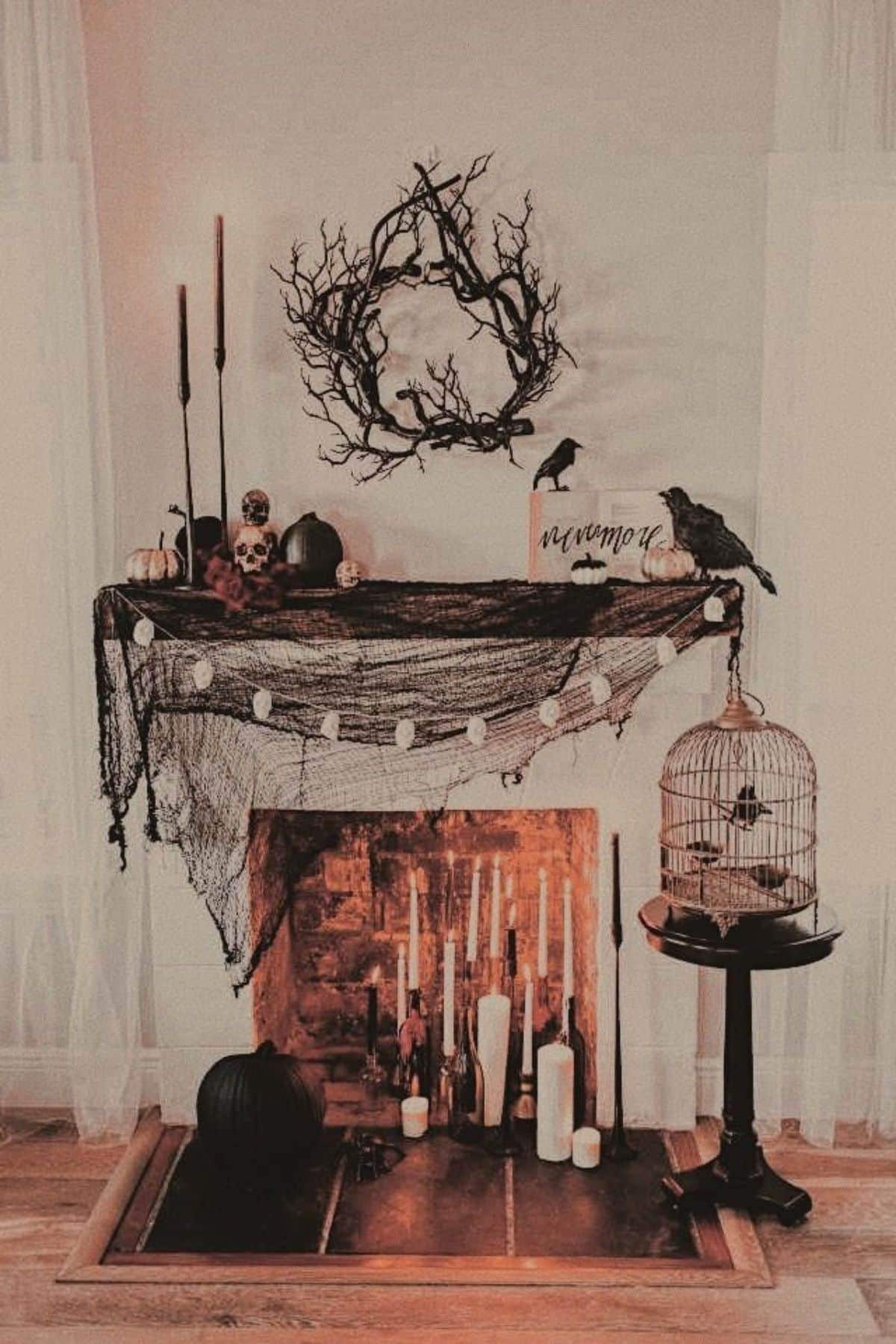 A fireplace decorated for Halloween with black netting, candles, skulls, pumpkins, a birdcage, crows, and a twisted branch wreath on the wall above the mantel.