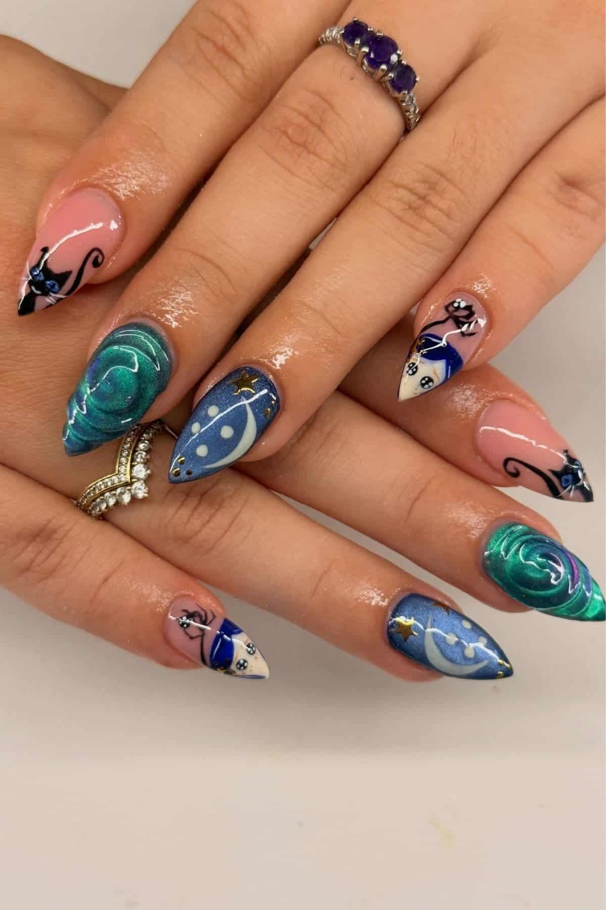 Hands with long, pointed nails featuring blue celestial and floral designs, including moons, stars, and swirls; fingers adorned with silver and gemstone rings.