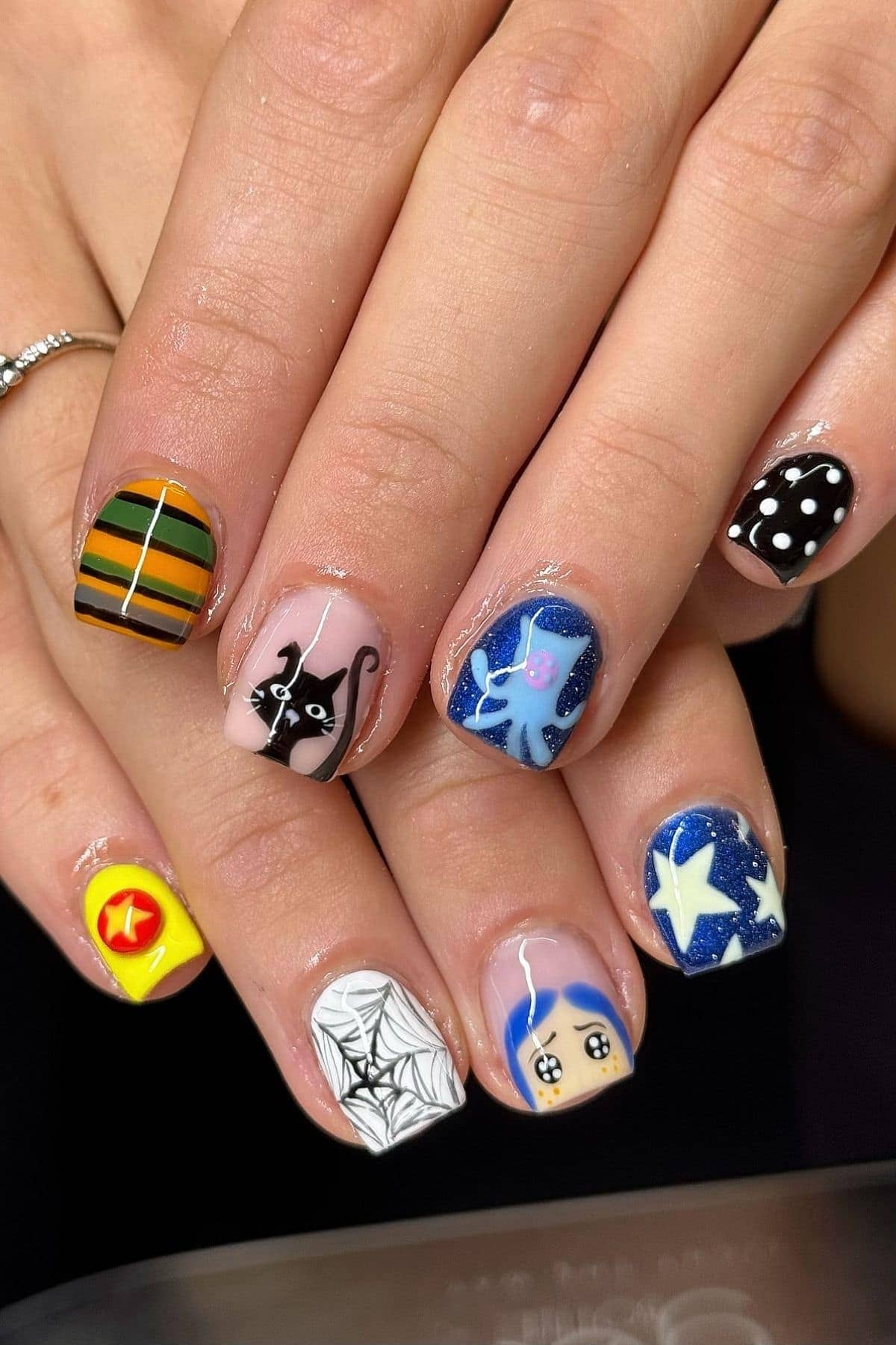 Fingernails with various designs, including stripes, polka dots, a black cat, an octopus, stars, a spider web, a cartoon face, and a yellow badge with a red star.