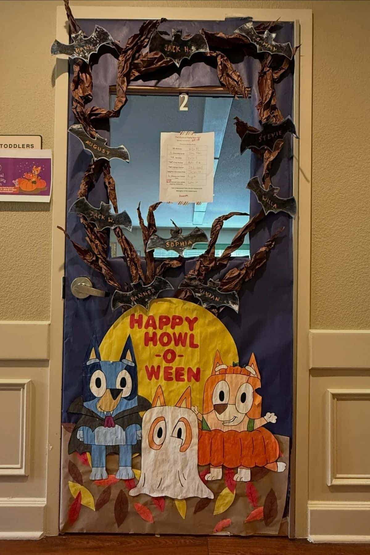 A classroom door decorated for Halloween with bats, branches, and cartoon animals in costumes. The words “Happy Howl-O-Ween” appear in yellow and orange on a moon background at the bottom.