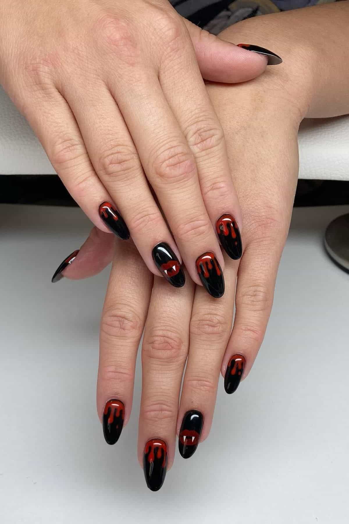 Hands with long, almond-shaped black nails featuring red drip designs on each nail, resting on a white surface.