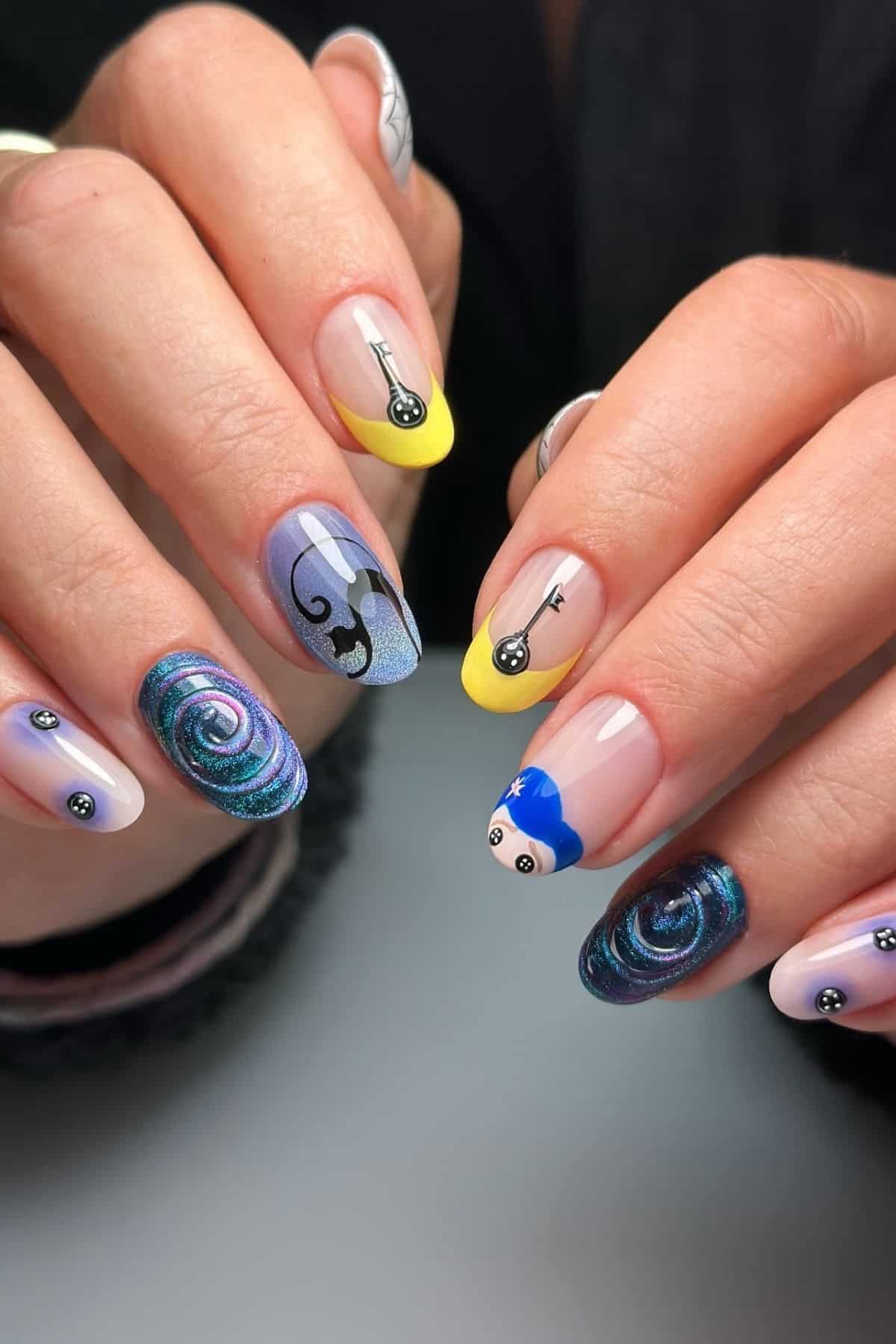 Hands with colorful nail art featuring a cat, swirls, yellow tips, a blue design, and small abstract elements on each fingernail.