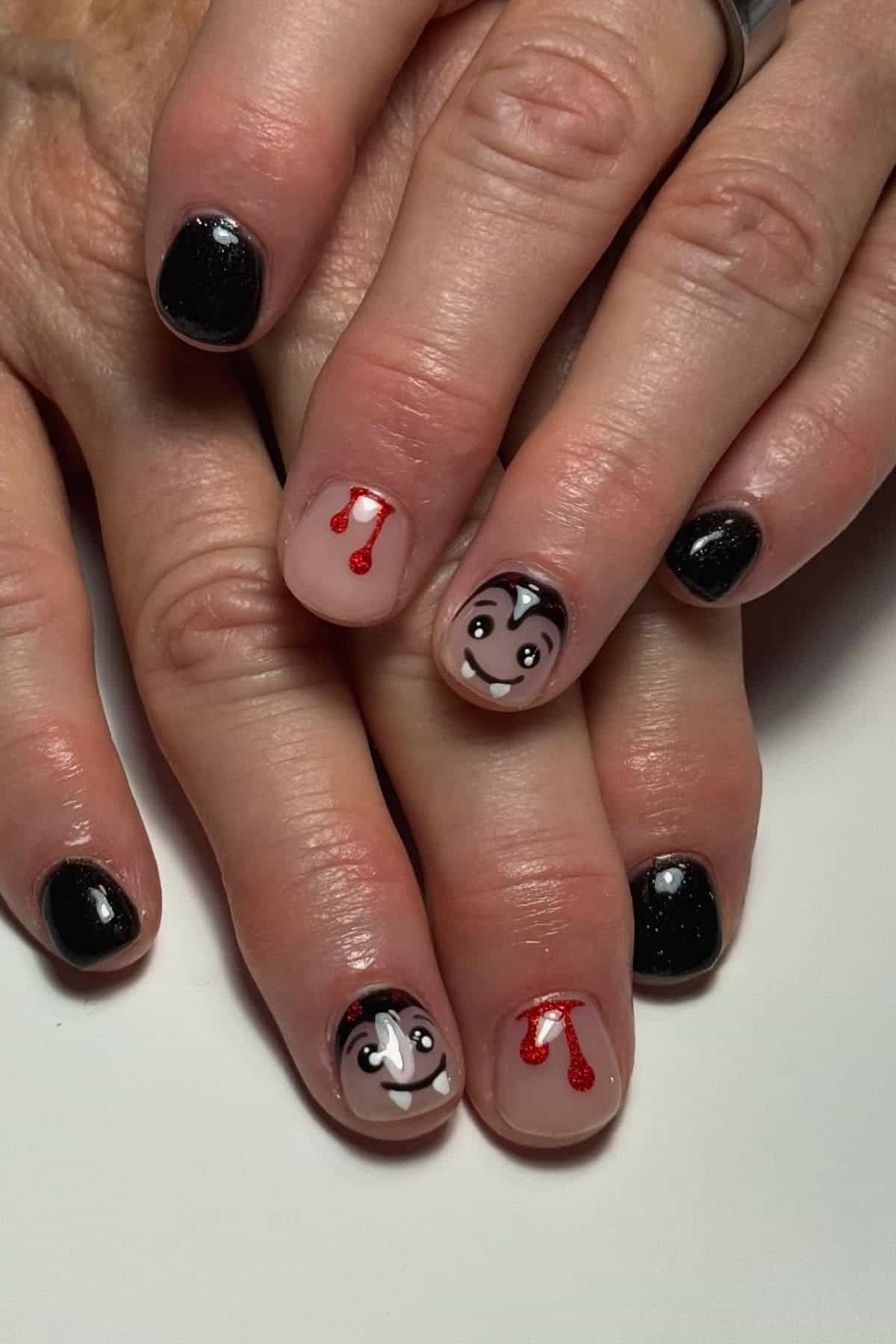 Hands with black nail polish; two nails have Dracula faces, two have painted blood drips, and the rest are solid black.