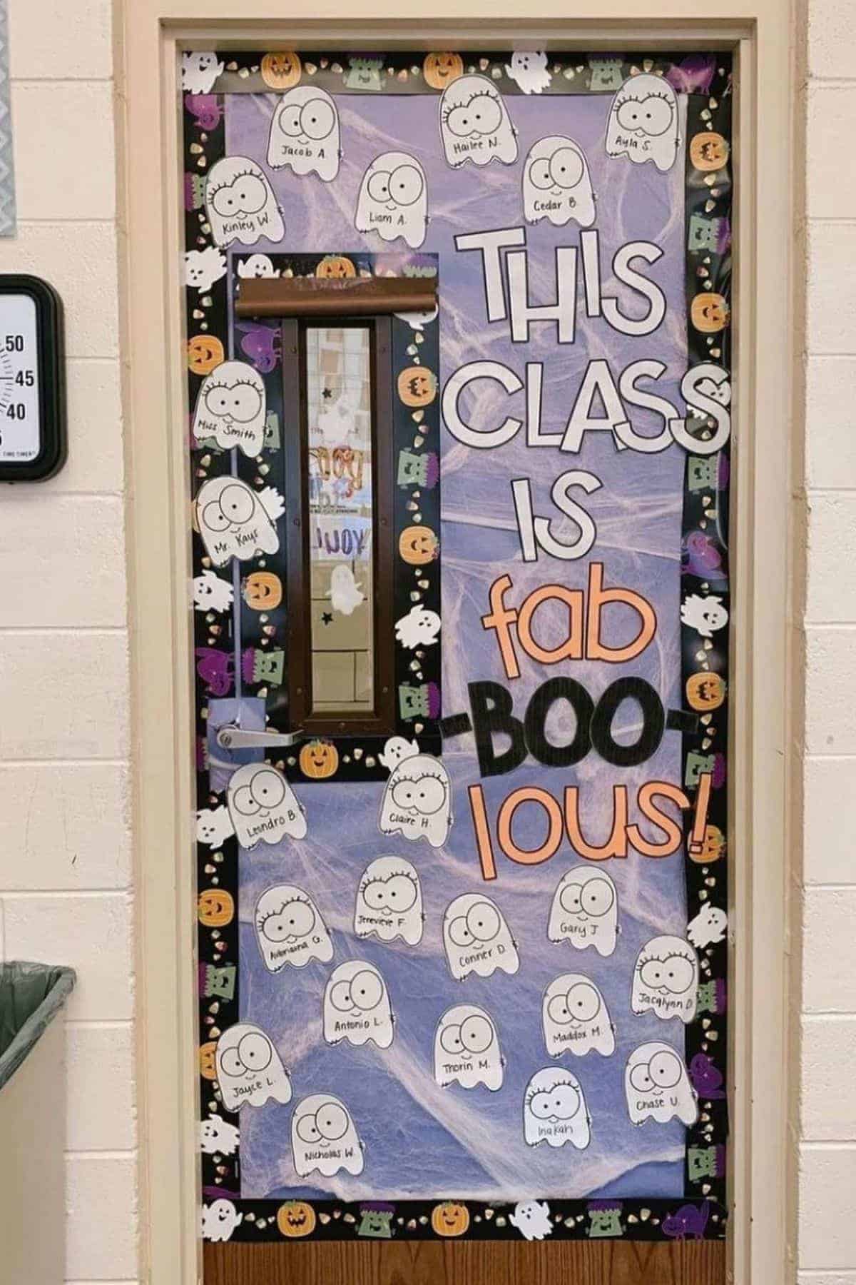 A classroom door decorated with ghost cutouts featuring names, pumpkin and bat borders, and the words “This class is fab-BOO-lous!” in large letters.