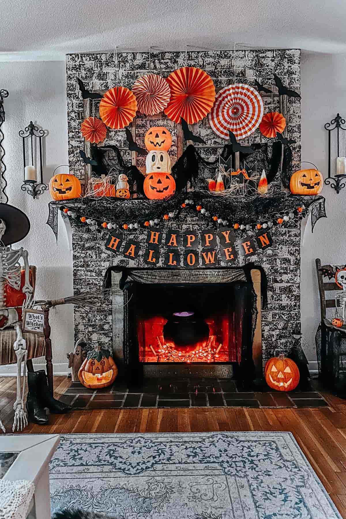 A decorated fireplace with jack-o’-lanterns, paper fans, spider webs, bats, and a “Happy Halloween” banner, creating a festive Halloween atmosphere.