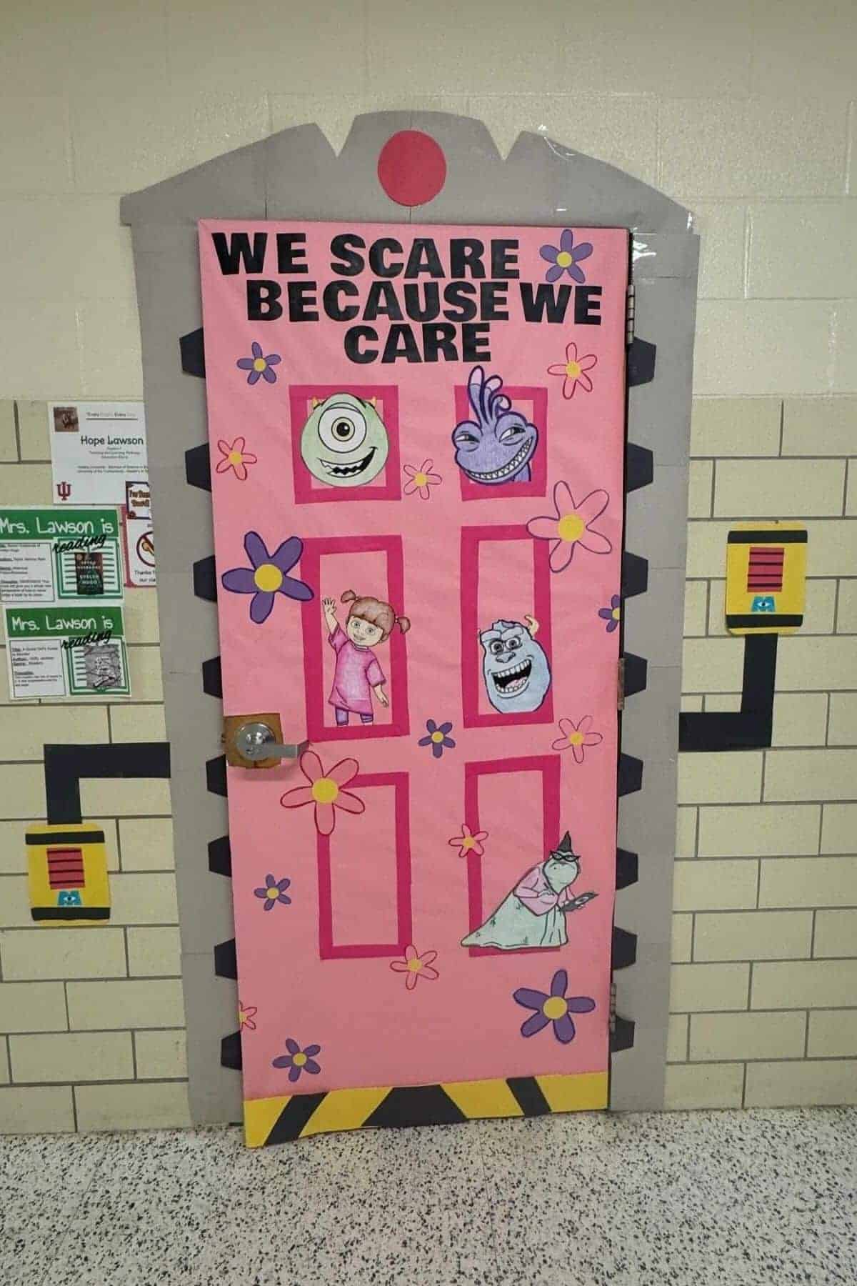 A classroom door decorated with Monsters, Inc. characters and the phrase “We scare because we care” on a pink background with flowers.