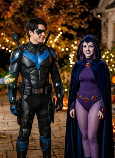 Four people in superhero costumes stand outside on a decorated path with pumpkins, string lights, and autumn leaves, smiling and talking at night.