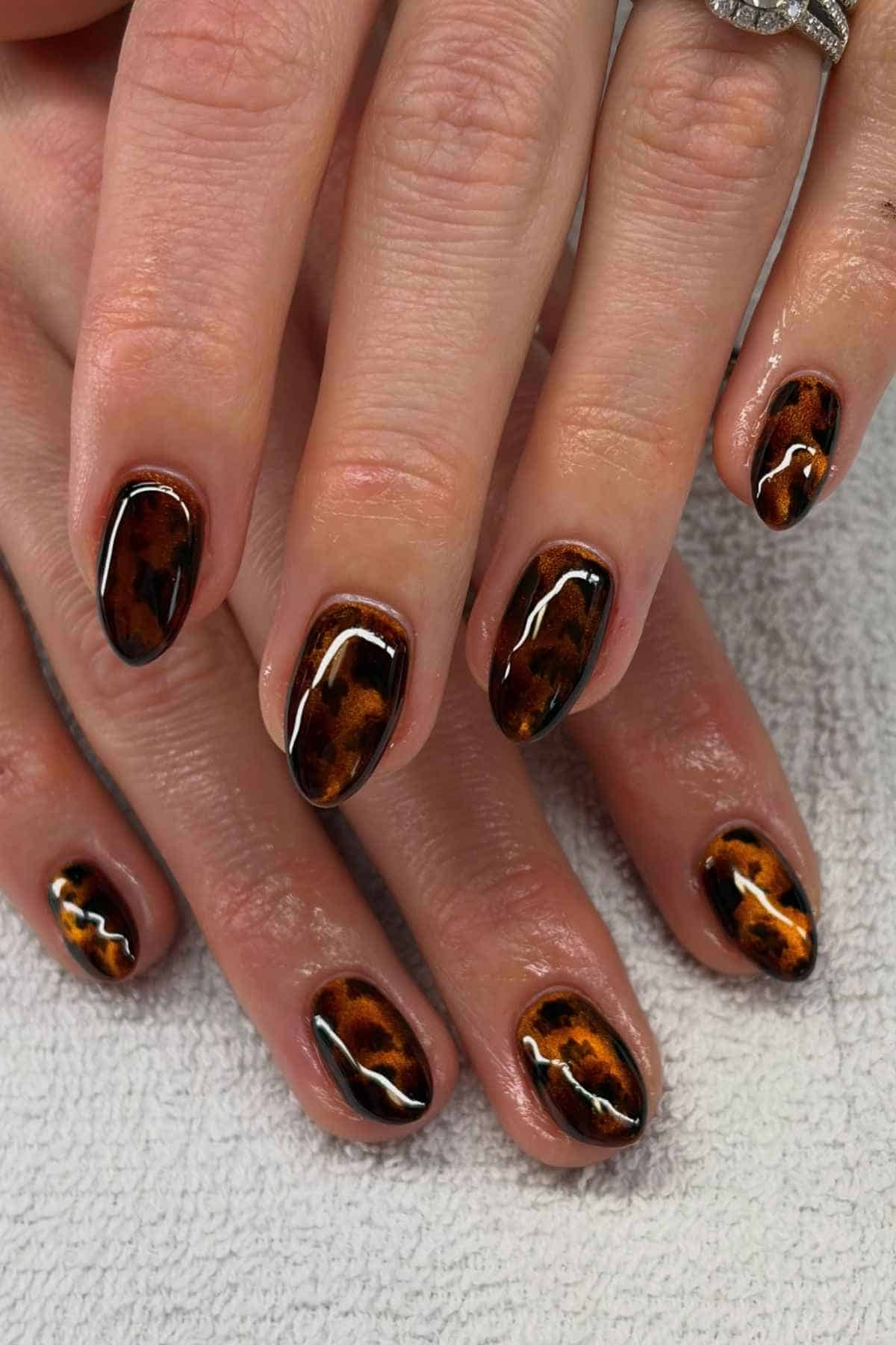 Hands with oval-shaped nails featuring a brown and black tortoiseshell pattern.