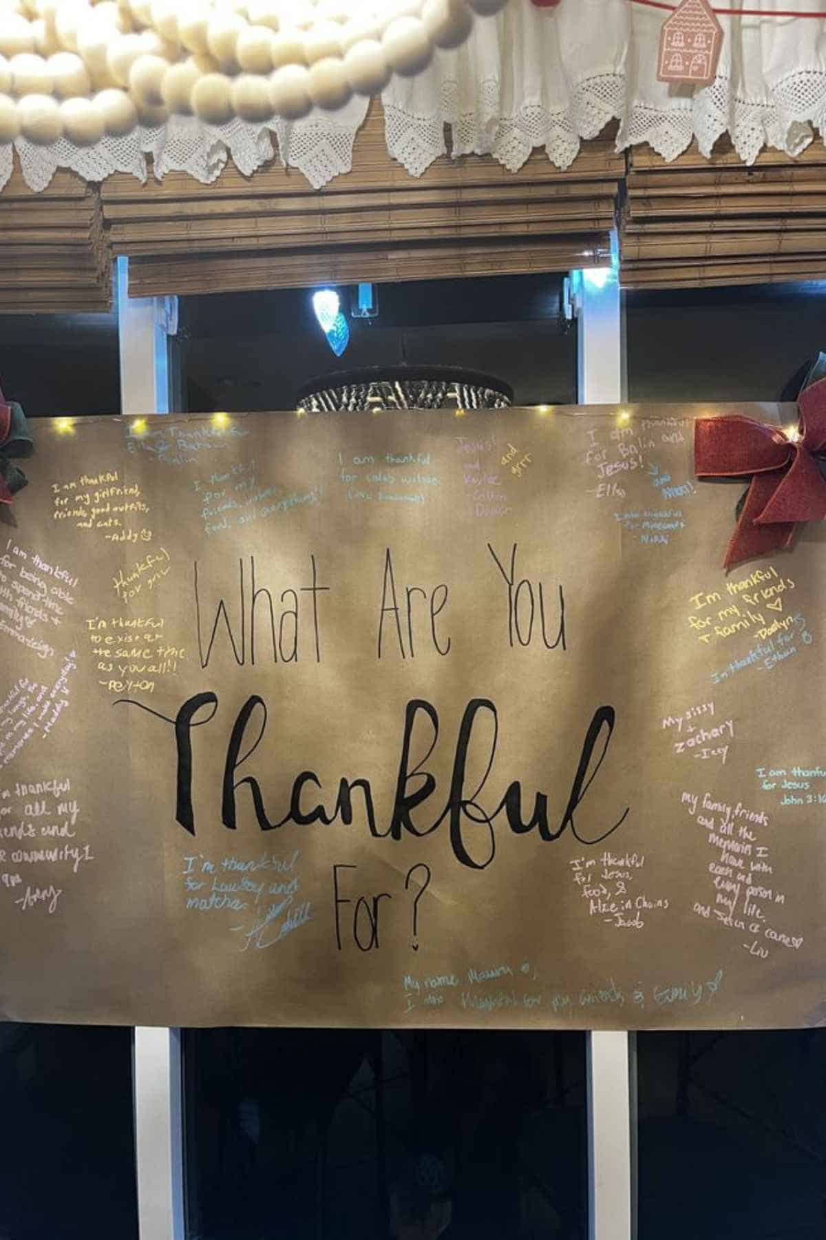 A large brown sign that reads “What Are You Thankful For?” with various handwritten notes of gratitude from different people.