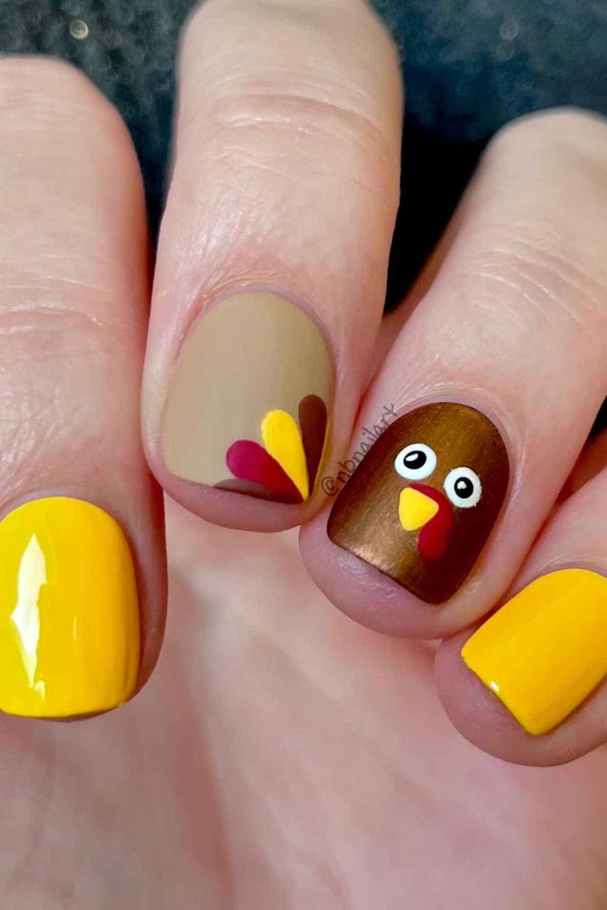 Fingernails painted with yellow polish and two accent nails featuring a turkey design and fall-colored feathers.