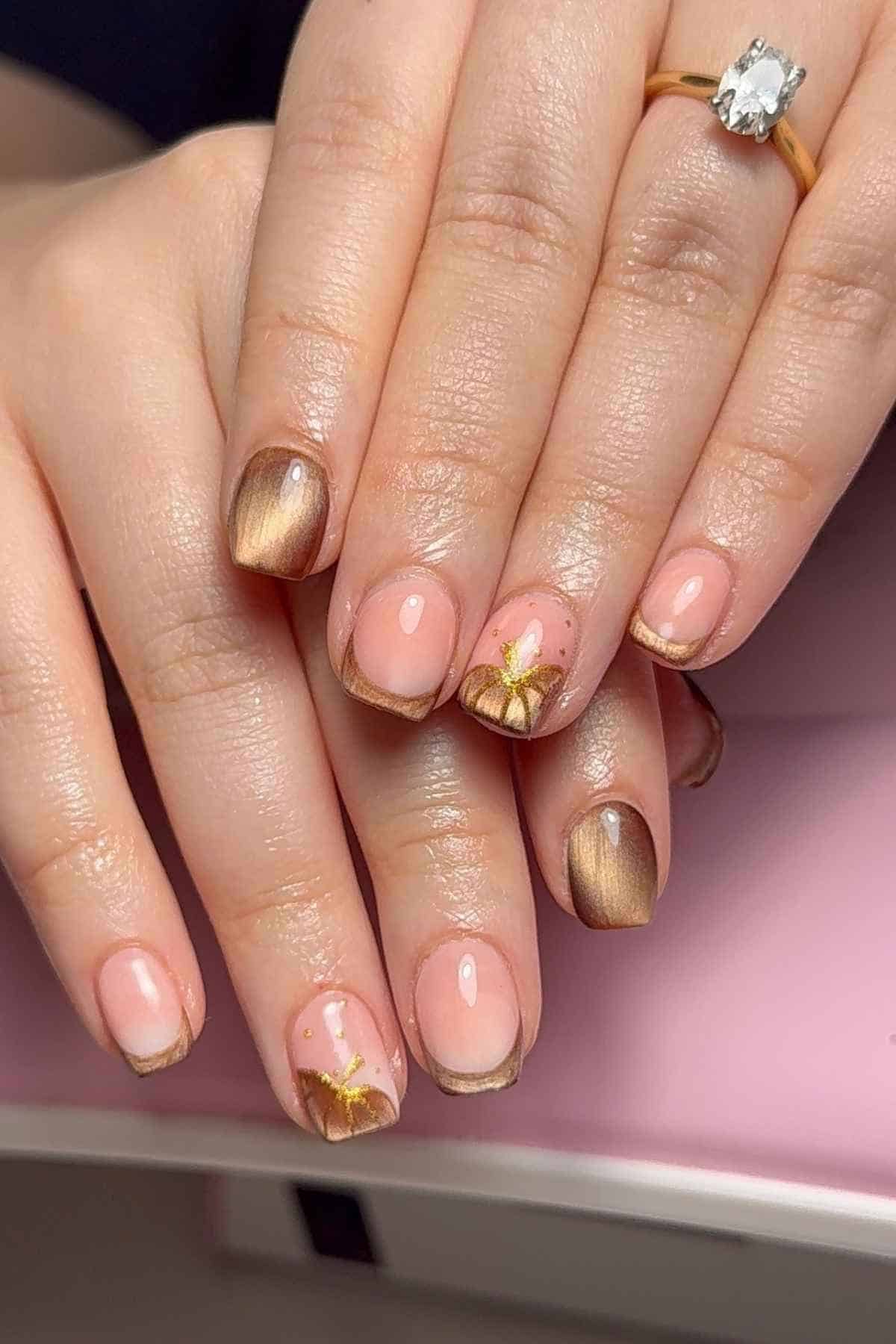 Short square nails with a pink base, gold tips, and metallic bronze accents, including a hand-painted gold flower on two fingers.