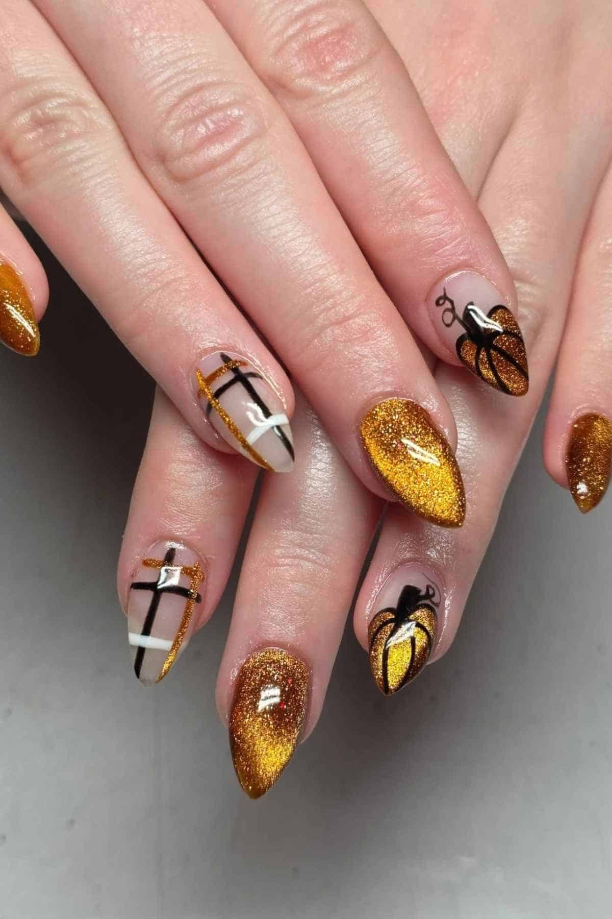 Manicured almond-shaped nails featuring gold glitter, black geometric cross designs, and small black pumpkin illustrations.