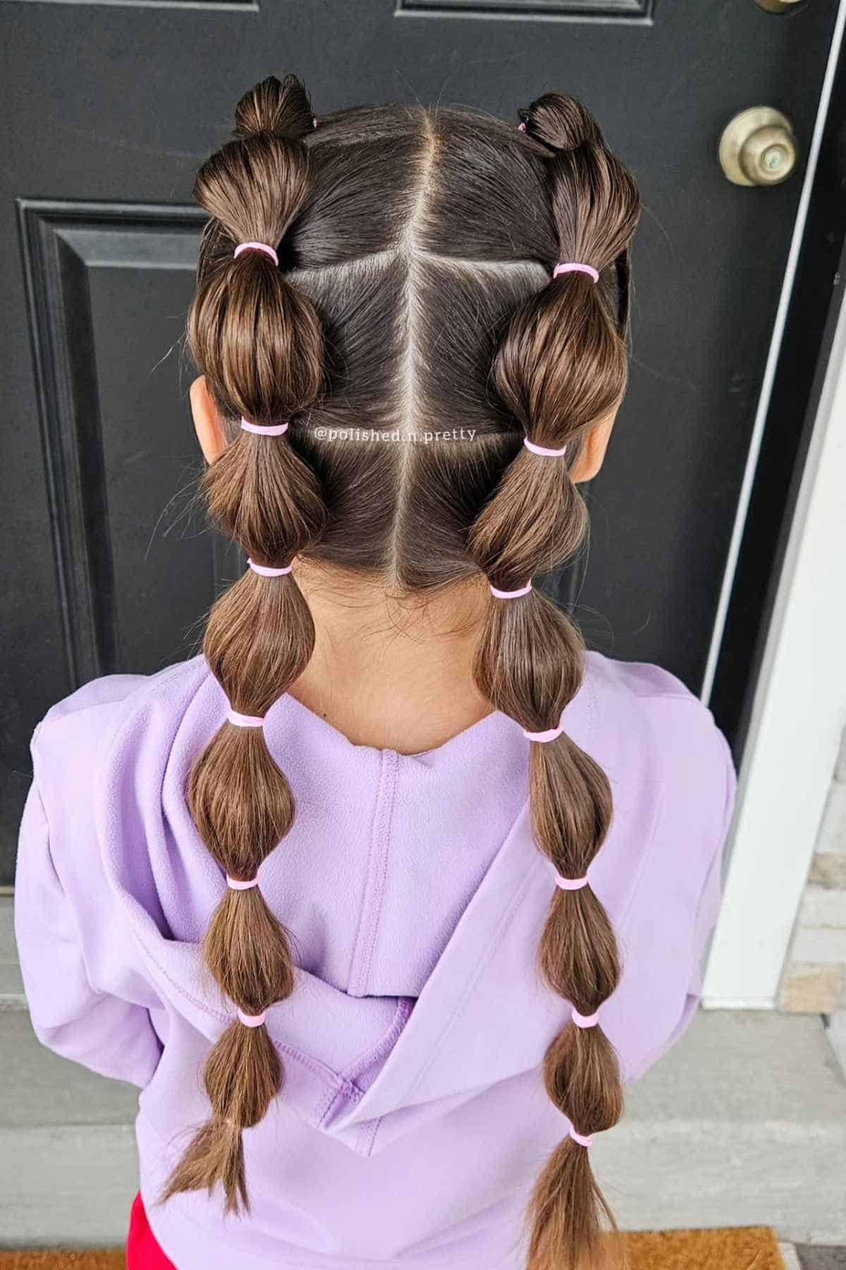 Back view of a person with hair styled in two long bubble braids using small pink elastics.