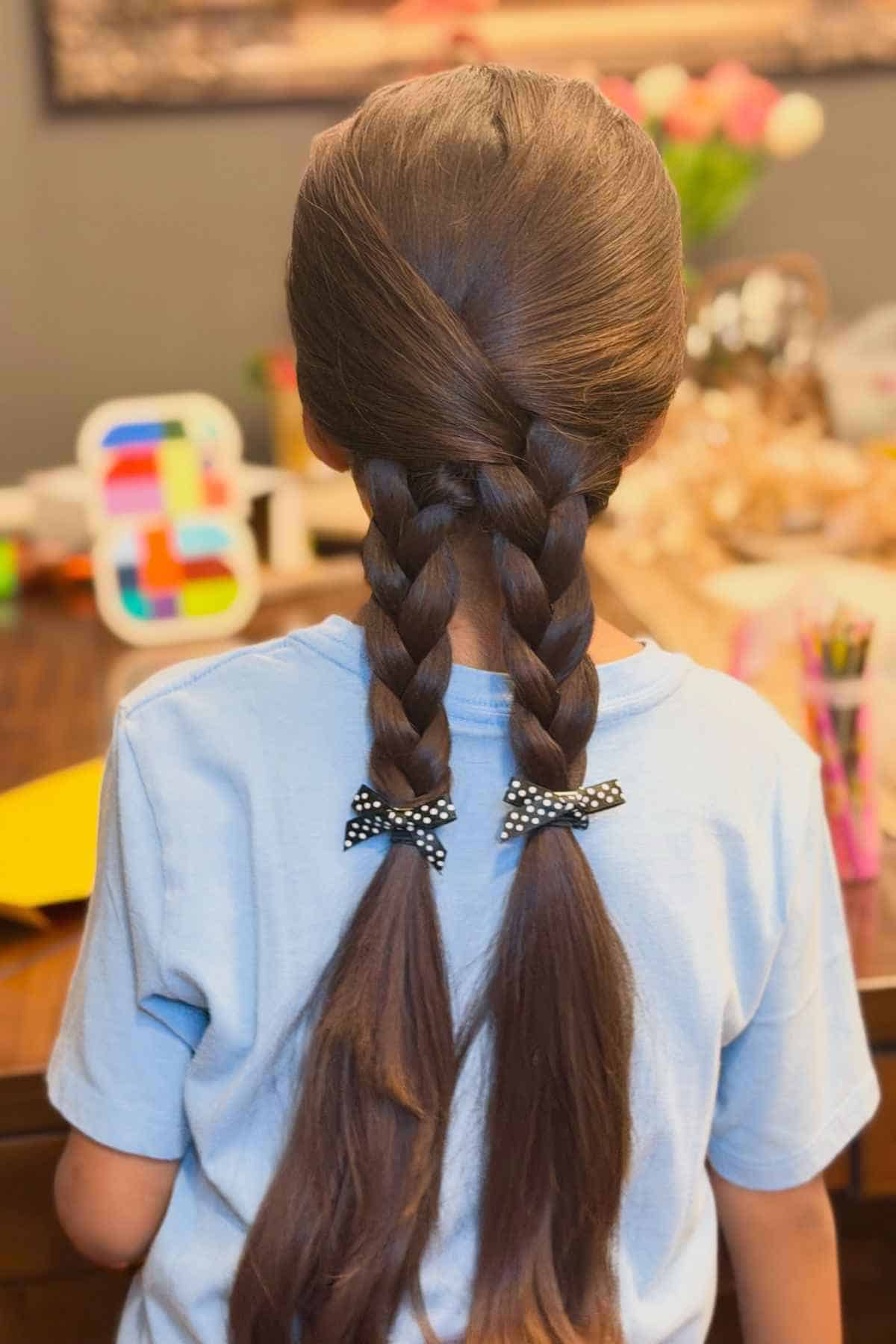 Back view of a child with brown hair styled in two braids tied with black and white polka-dot bows.