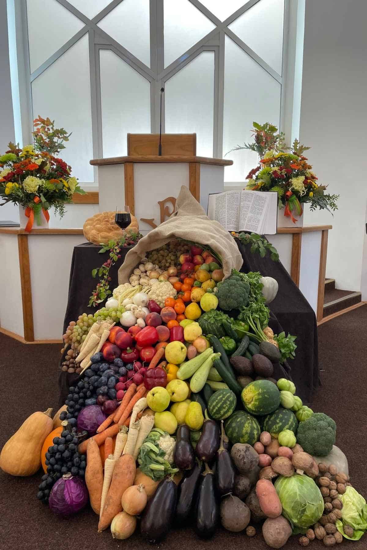 A large cornucopia overflowing with a variety of fresh fruits and vegetables on a table in front of a church altar.