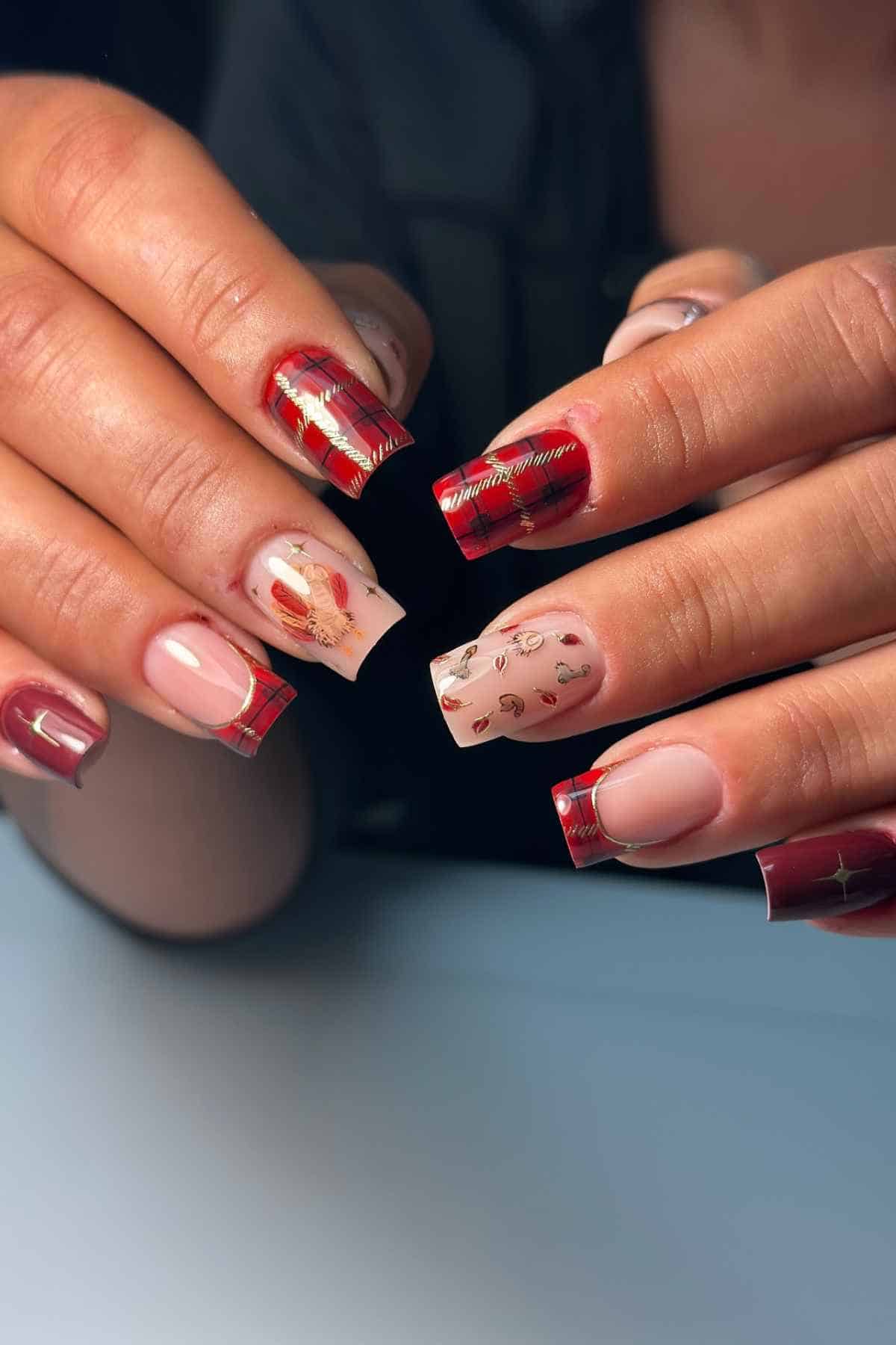 Manicured nails featuring red plaid patterns, French tips, and small gold leaf decals.