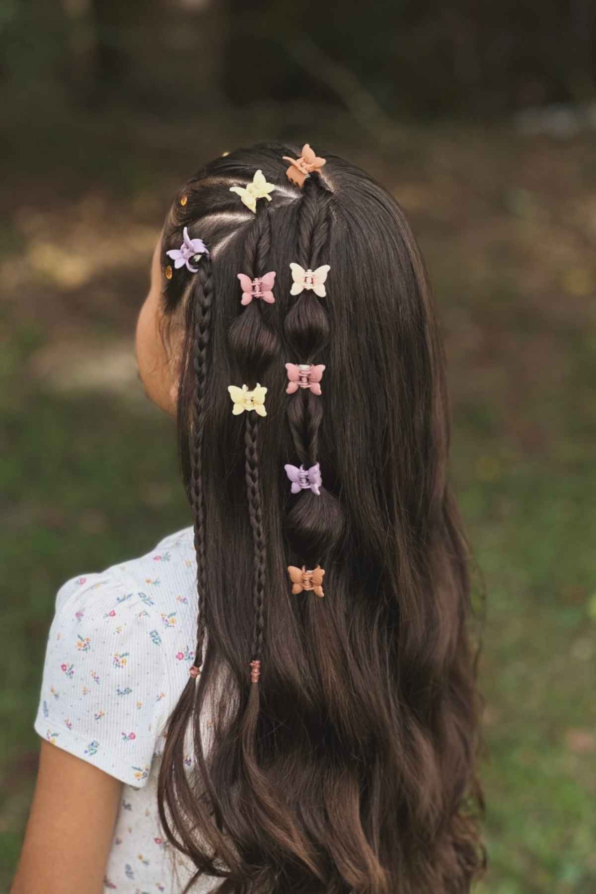 A person’s long brown hair styled in a half-up ponytail with small, colorful butterfly-shaped hair clips.