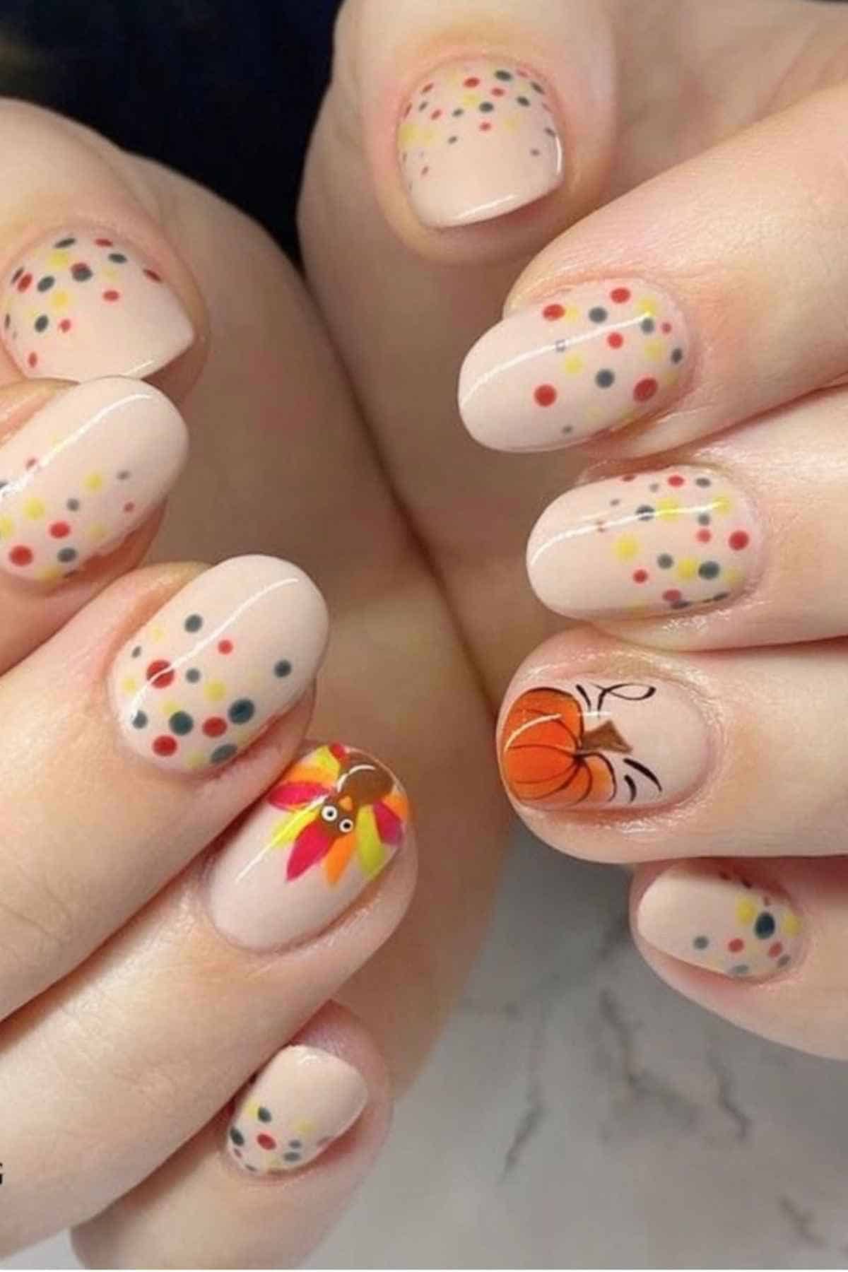 Nude-colored manicured fingernails with colorful dots, a painted turkey, and a pumpkin design.