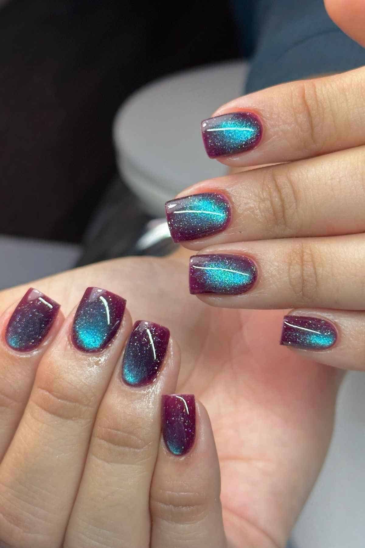 Short, square-shaped fingernails featuring a magnetic cat-eye polish with a purple base and a vibrant teal shimmer.