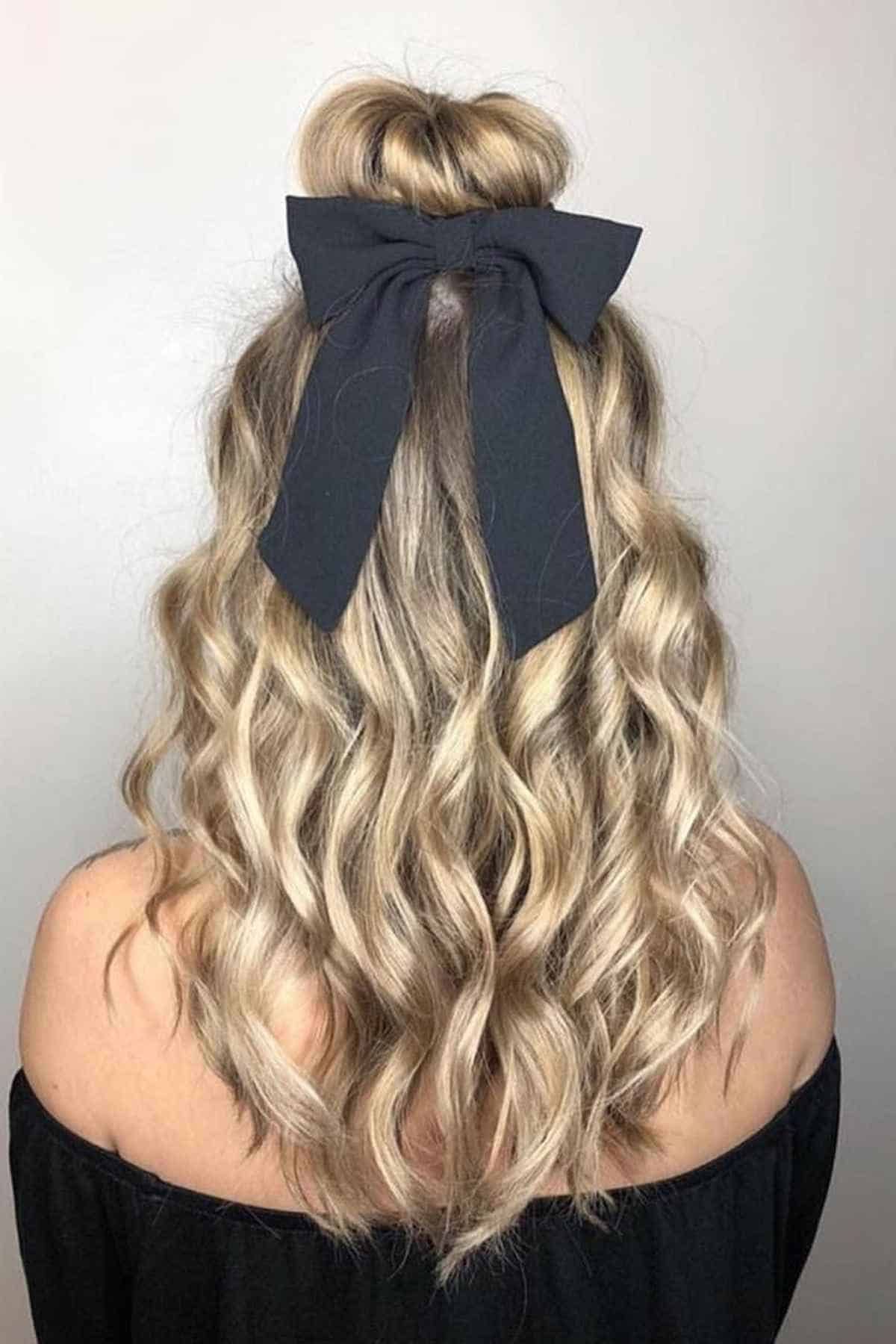 A person with long, blonde, wavy hair styled in a half-up bun secured with a black fabric bow.